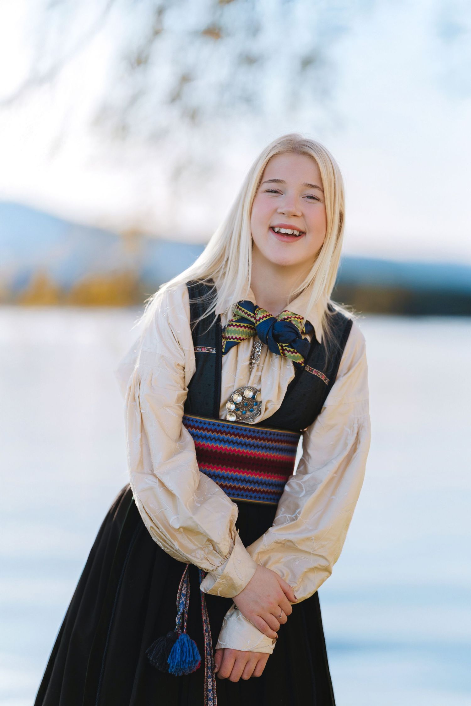 Person wearing traditional Norwegian folk dress laughs joyfully against snowy winter backdrop.