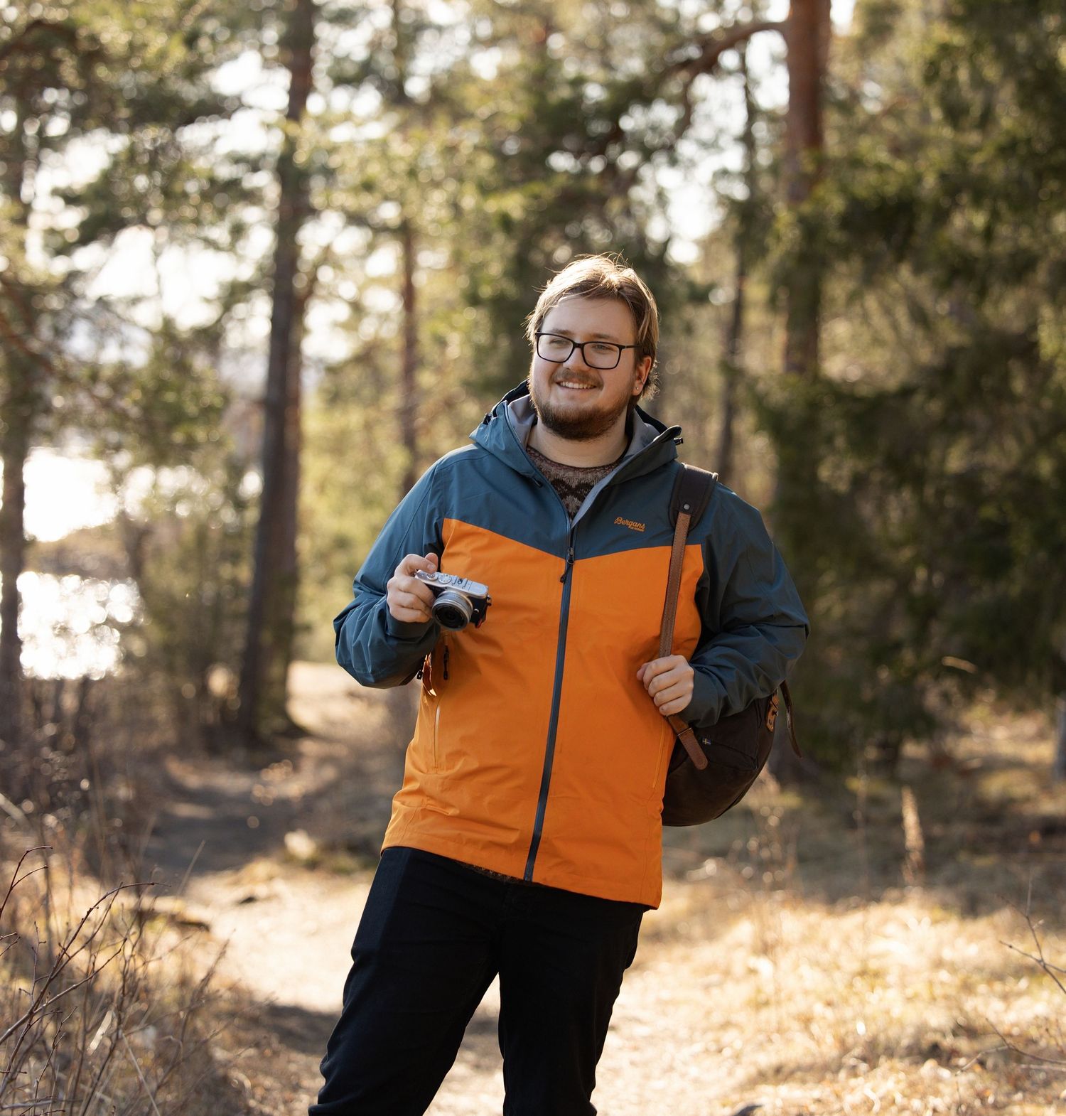A person wearing an orange and navy winter jacket poses outdoors in a snowy forest setting.