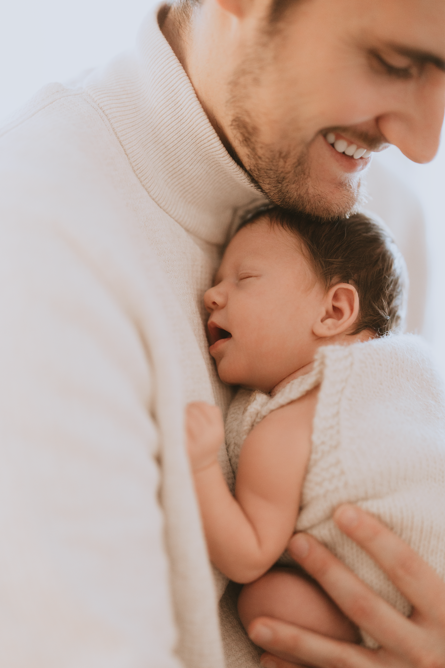 A tender moment between parent and sleeping newborn baby wrapped in soft white blankets.