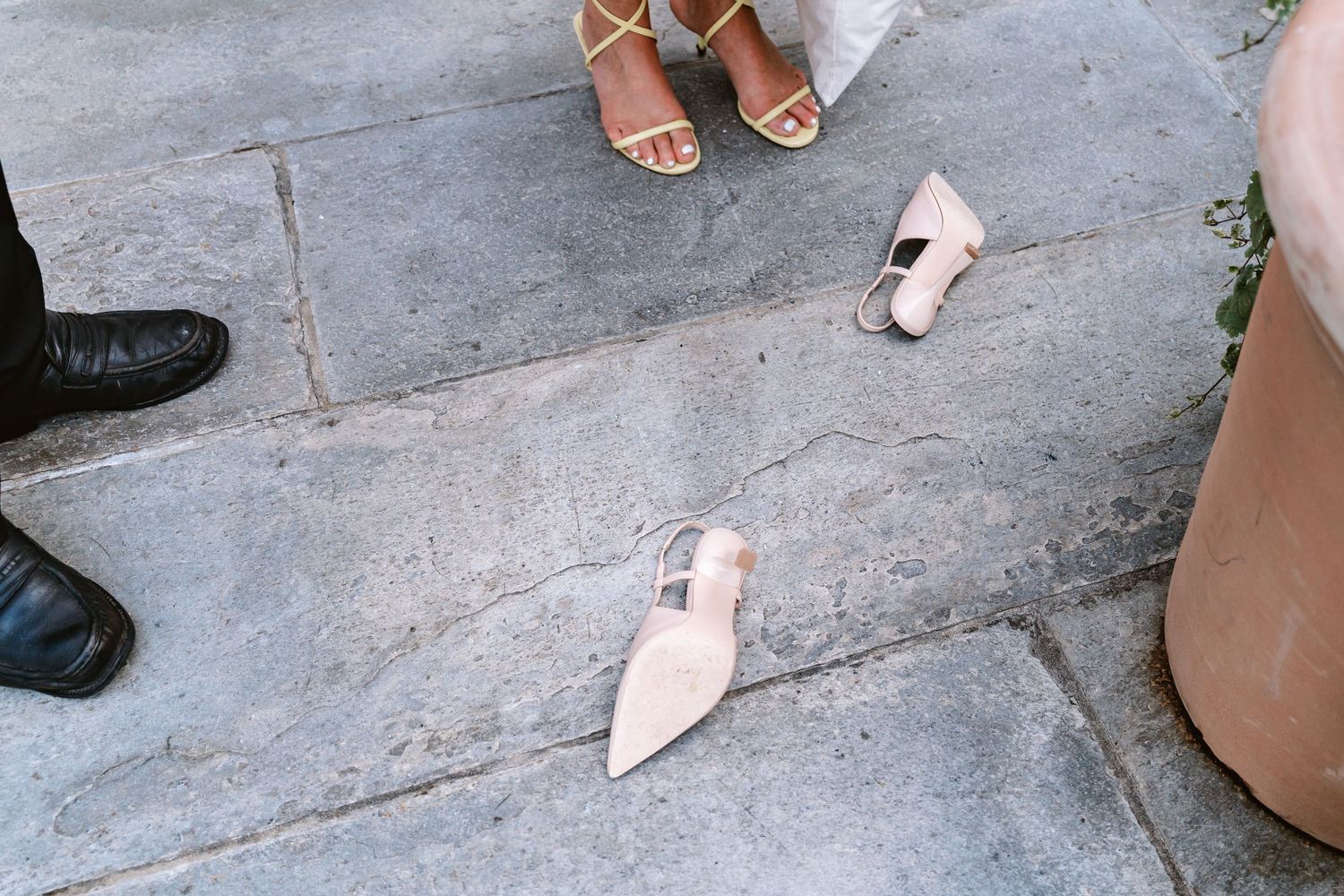 Stylish footwear including black dress shoes and nude pointed flats arranged on gray stone pavement.