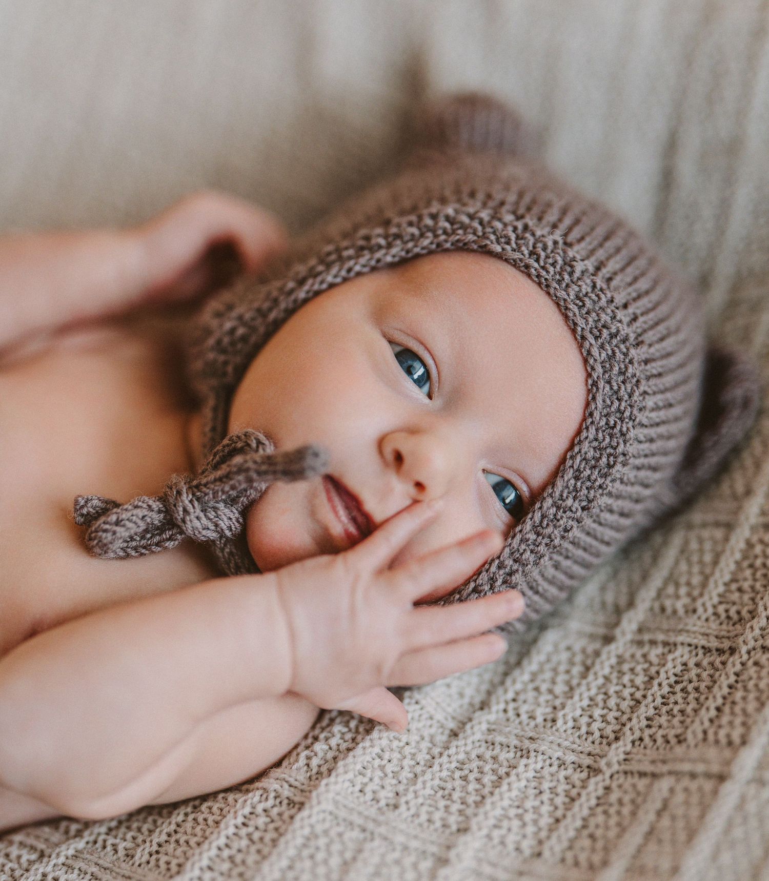 Close up of baby in gray knitted hat resting on beige textured blanket.
