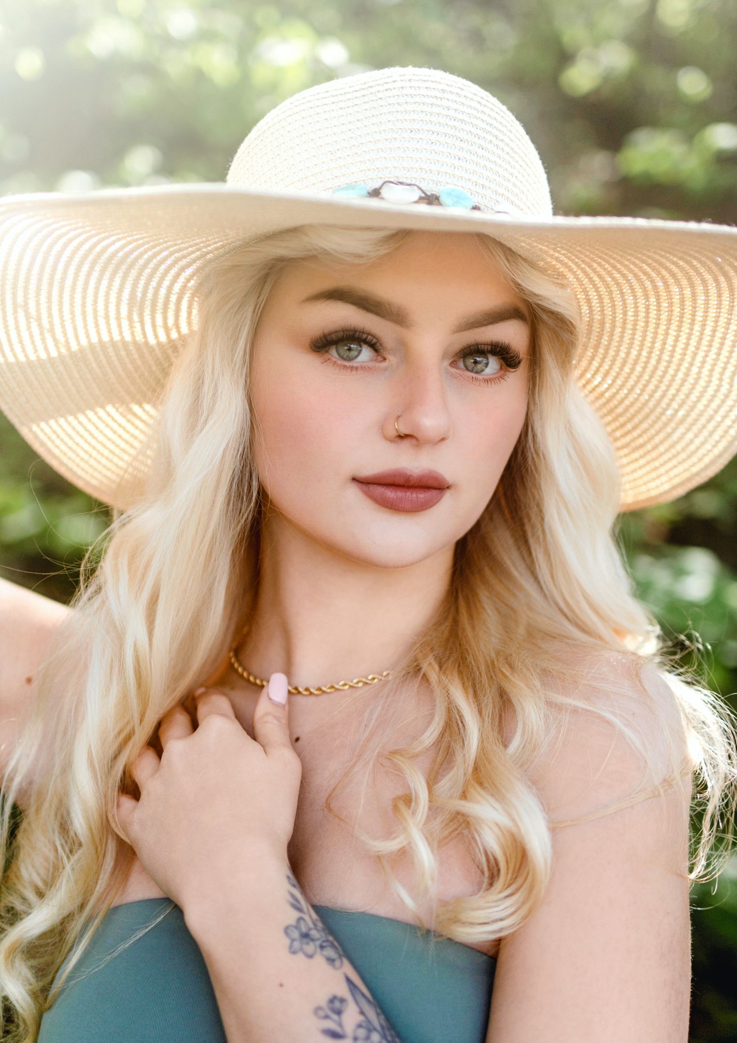Woman wearing wide-brimmed sun hat and teal top in outdoor summer portrait.