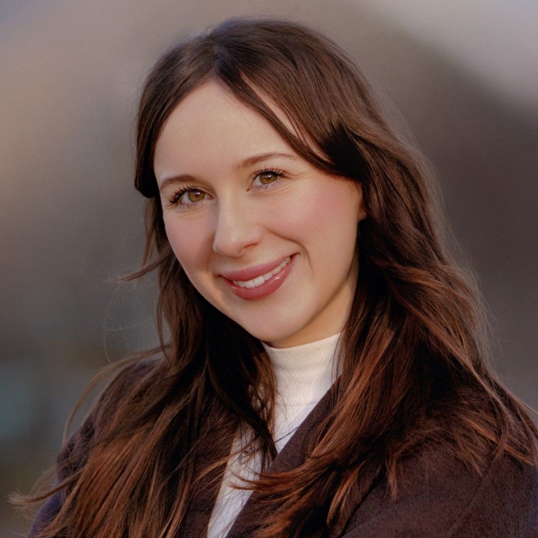 A woman with long brown hair and a white turtleneck smiles warmly at the camera in a professional headshot.