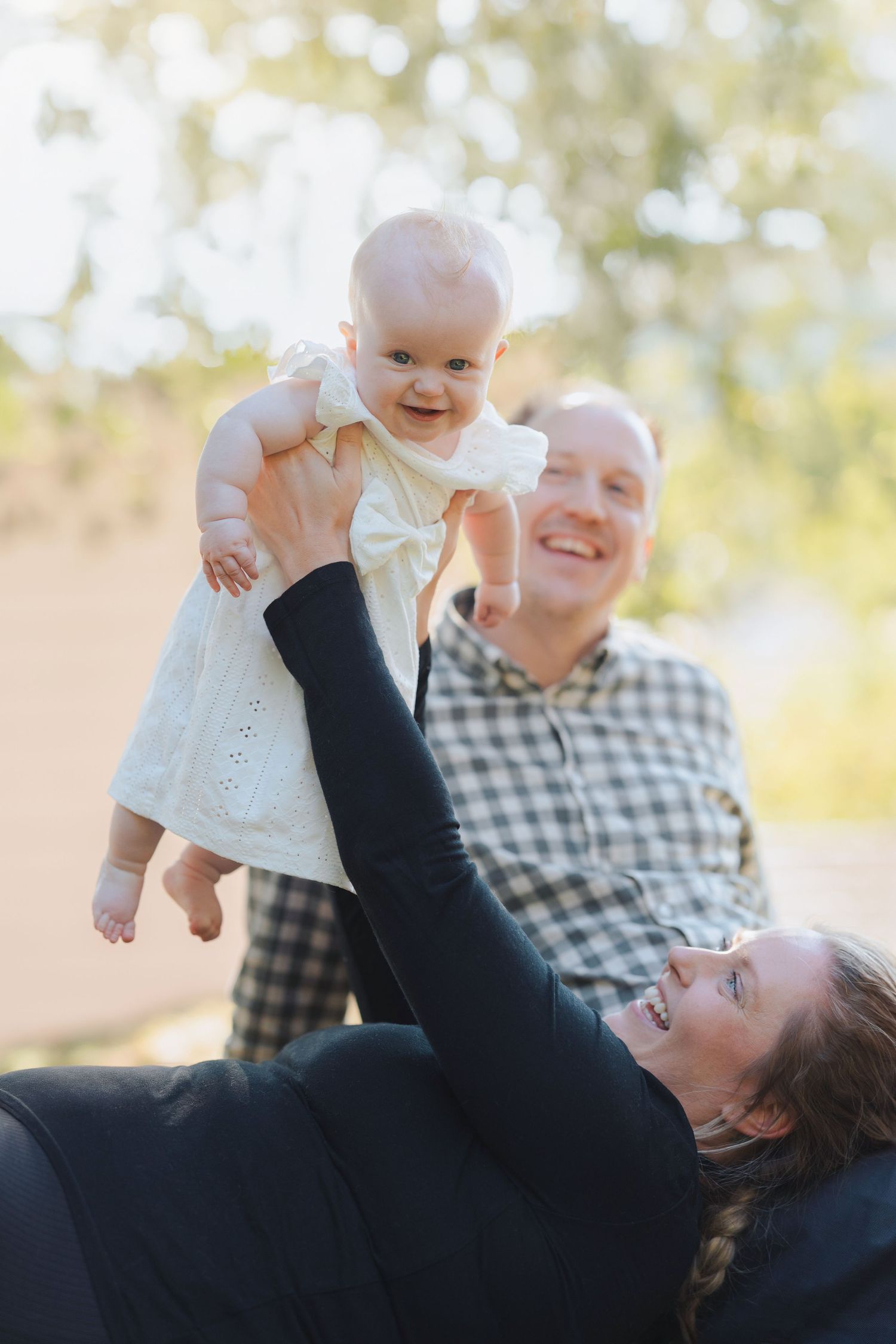 A series of joyful moments captured as a baby in a white dress is lifted playfully into the air outdoors.