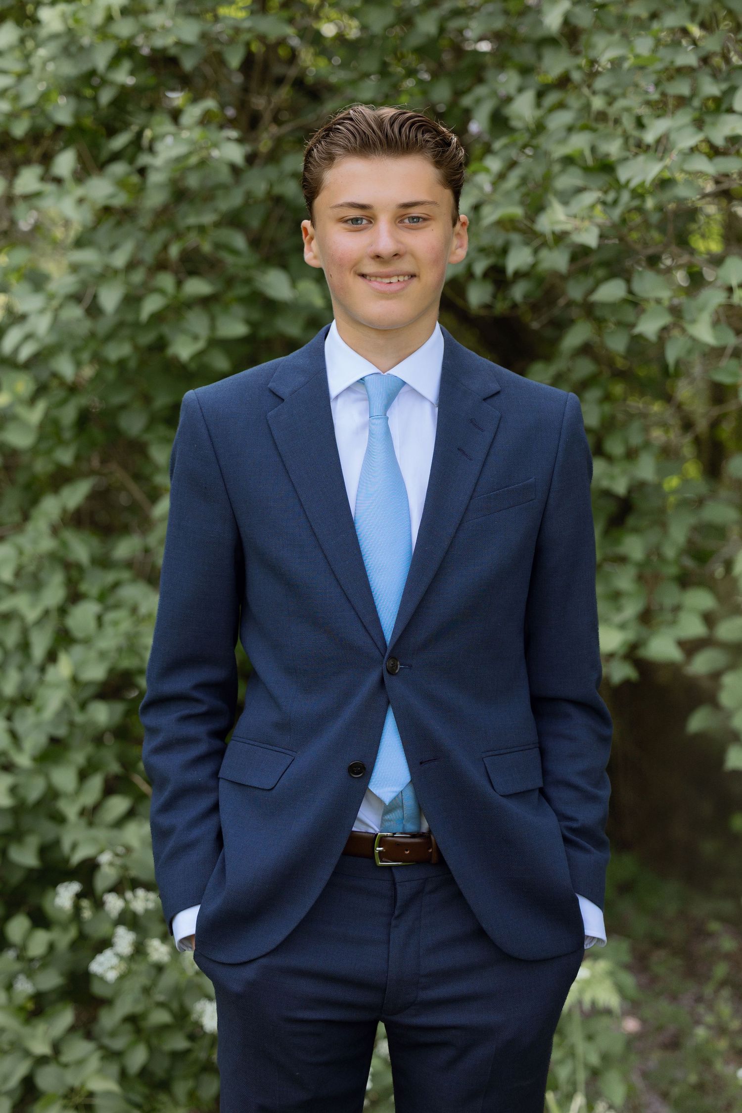 A series of formal portraits showing someone in a navy suit and light blue tie against a leafy green background.