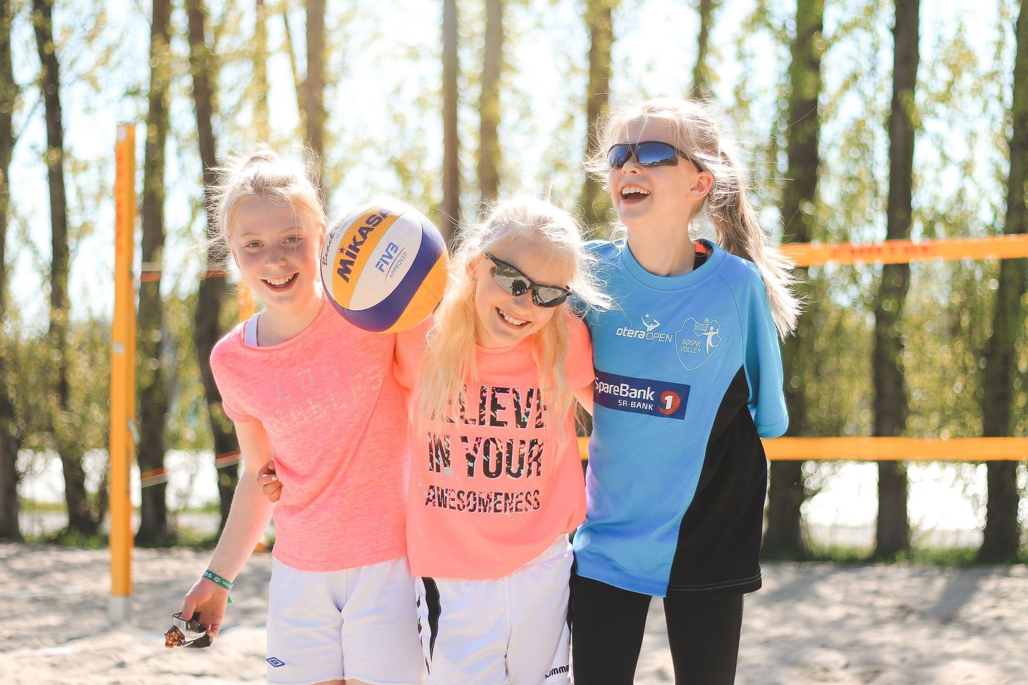 A group of runners smiling and jogging together on a wooded trail during a sunny day.