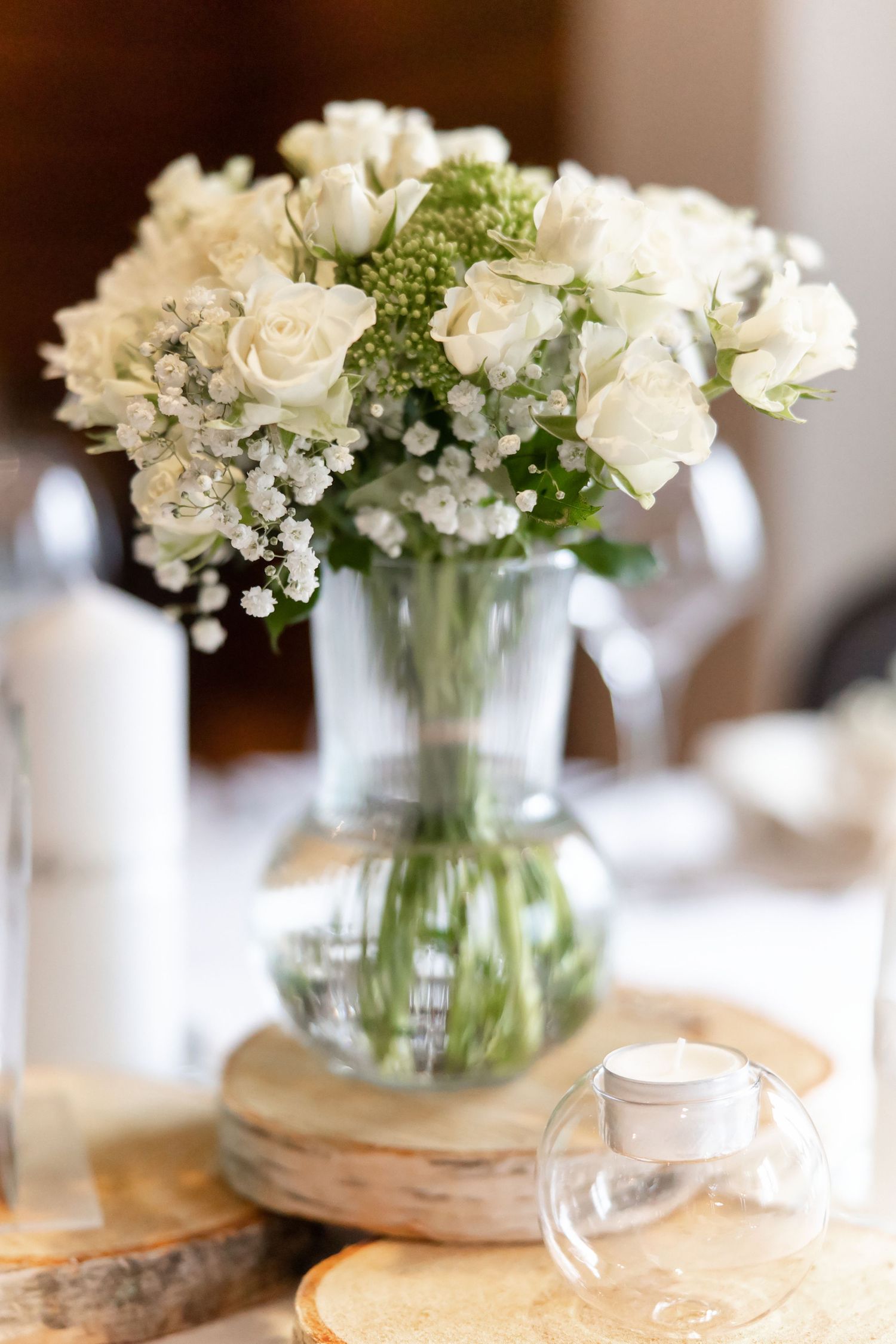 White carnations and baby's breath flowers arranged in clear glass mason jars create an elegant rustic centerpiece display.