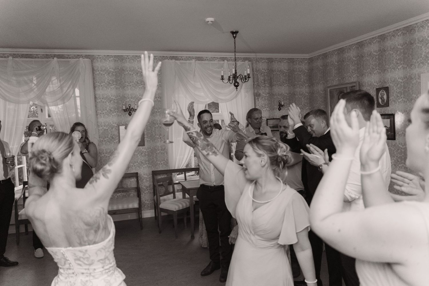 Wedding guests dancing and raising their hands on the dance floor during a celebration at a reception venue.