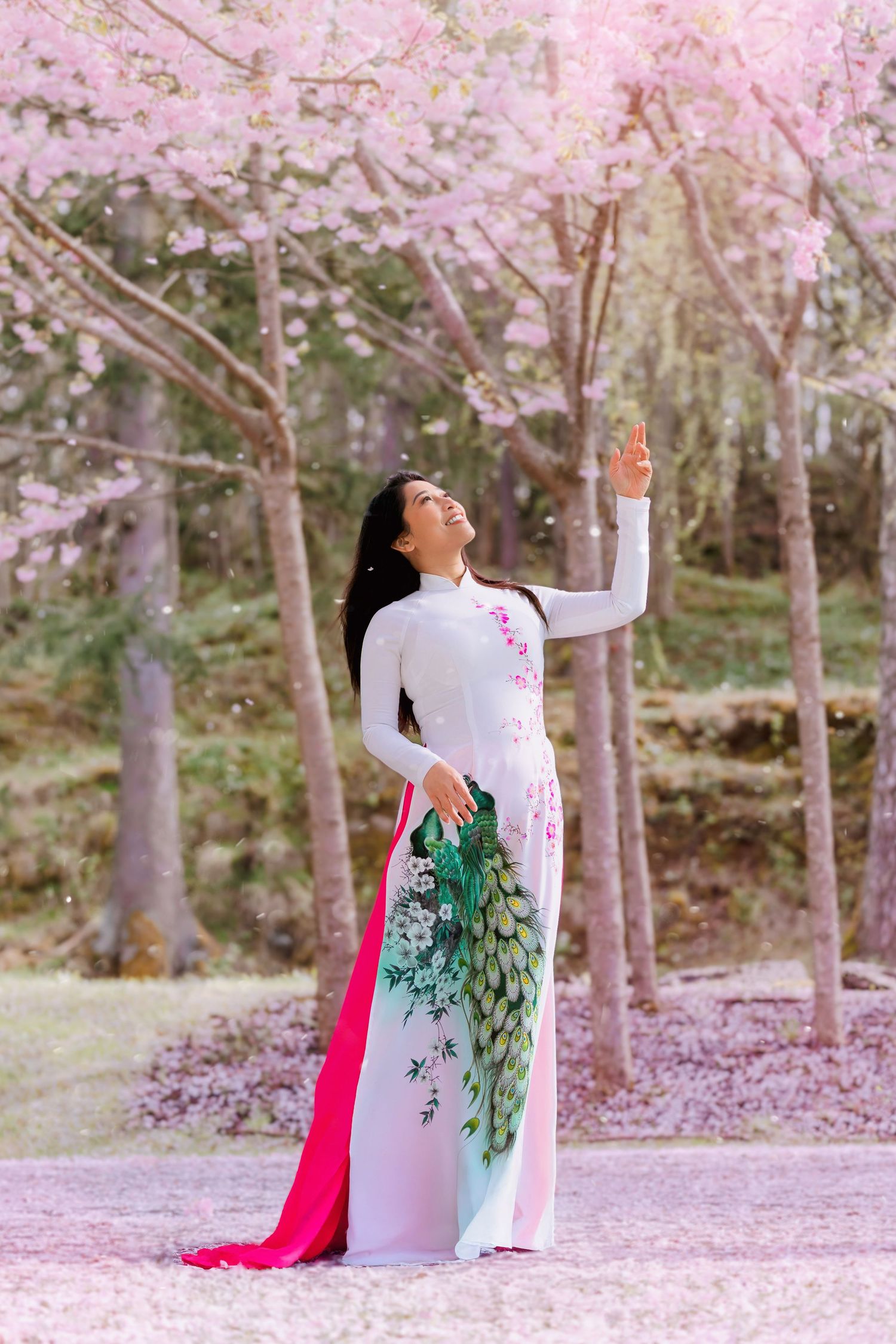 A figure in a flowing white traditional dress with green embroidery spins gracefully among cherry blossom trees in spring.
