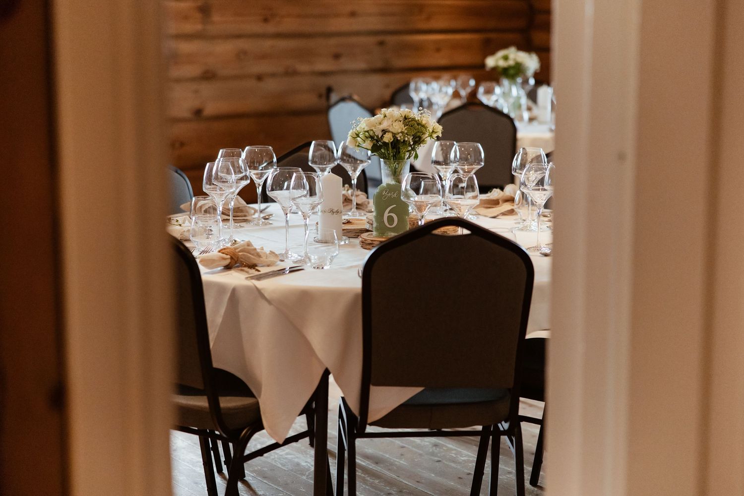An elegant dining room setup with white tablecloths, formal place settings and crystal glasses in a warm-lit restaurant interior.