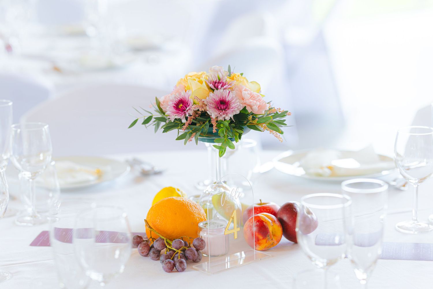 Elegant table setting with fresh flowers, citrus fruits, and glassware arranged on a white tablecloth.