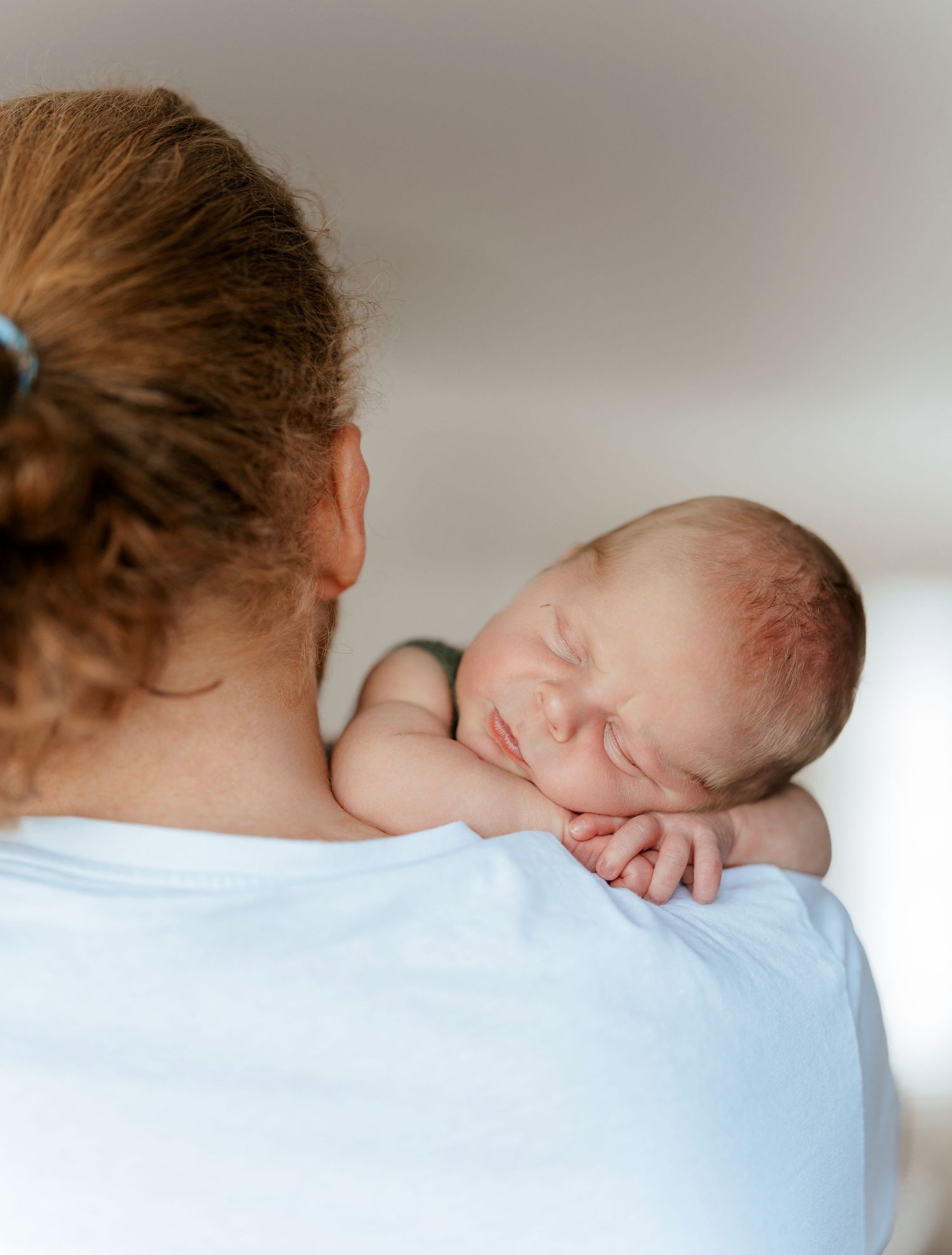 A newborn baby sleeping peacefully on a parent's shoulder, cradled gently in a tender bonding moment.