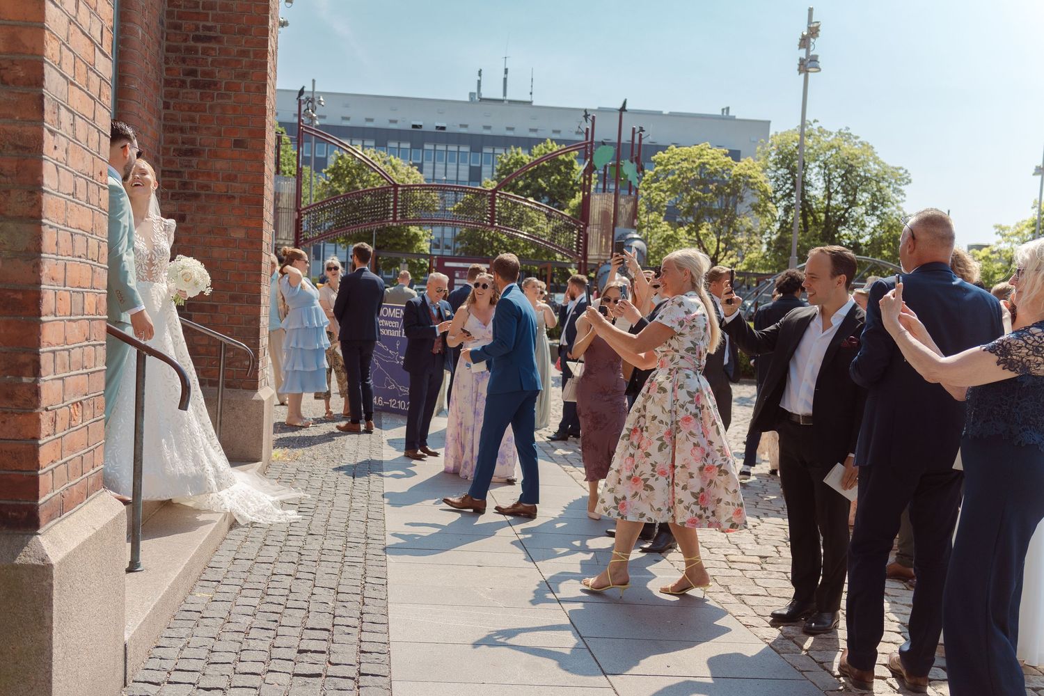 Musicians perform outdoors with brass instruments along a brick walkway at a sunny daytime event.