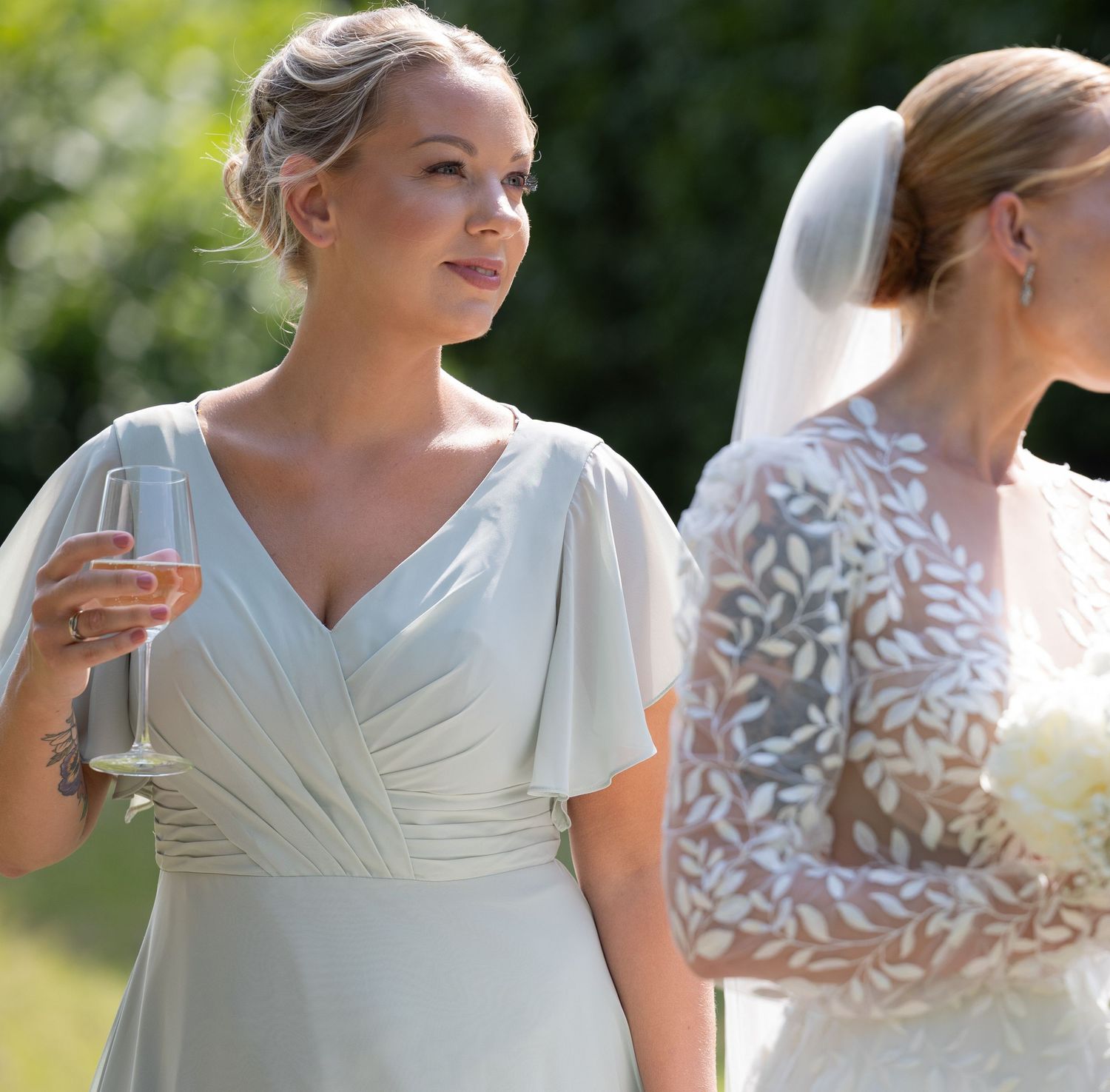 A person in a white wedding dress with short sleeves poses outdoors in a garden setting.