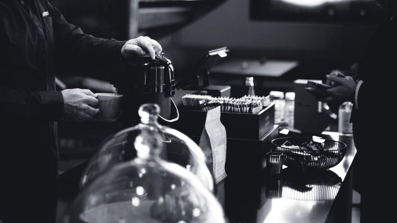 Black and white image of hands operating an espresso machine in a dark setting.