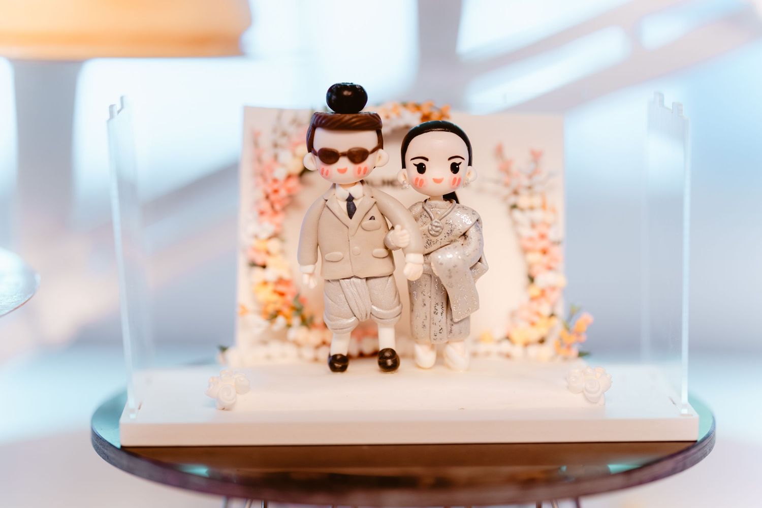 Cute wedding cake topper figurines displayed on a wooden surface with pink and white floral decorations.