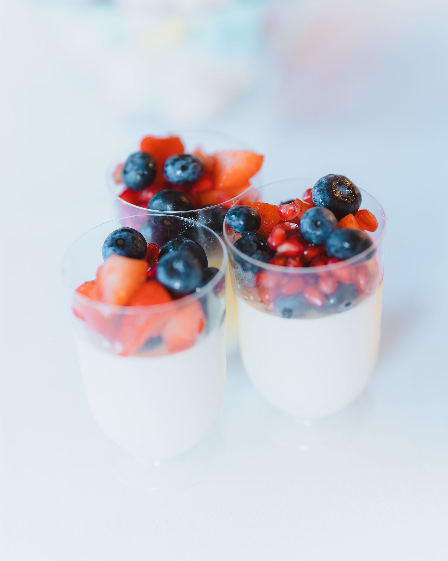 Fresh blueberries and strawberry slices arranged in small white ceramic bowls on a light background.