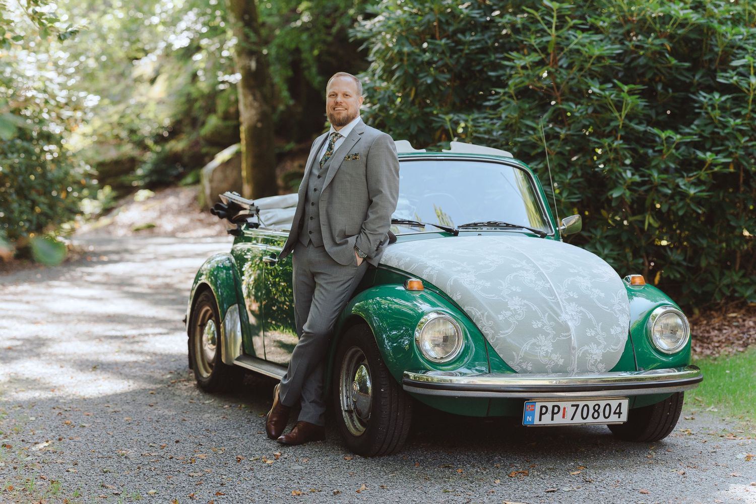 A vintage green Citroen DS car parked in a wooded area with someone standing beside it.