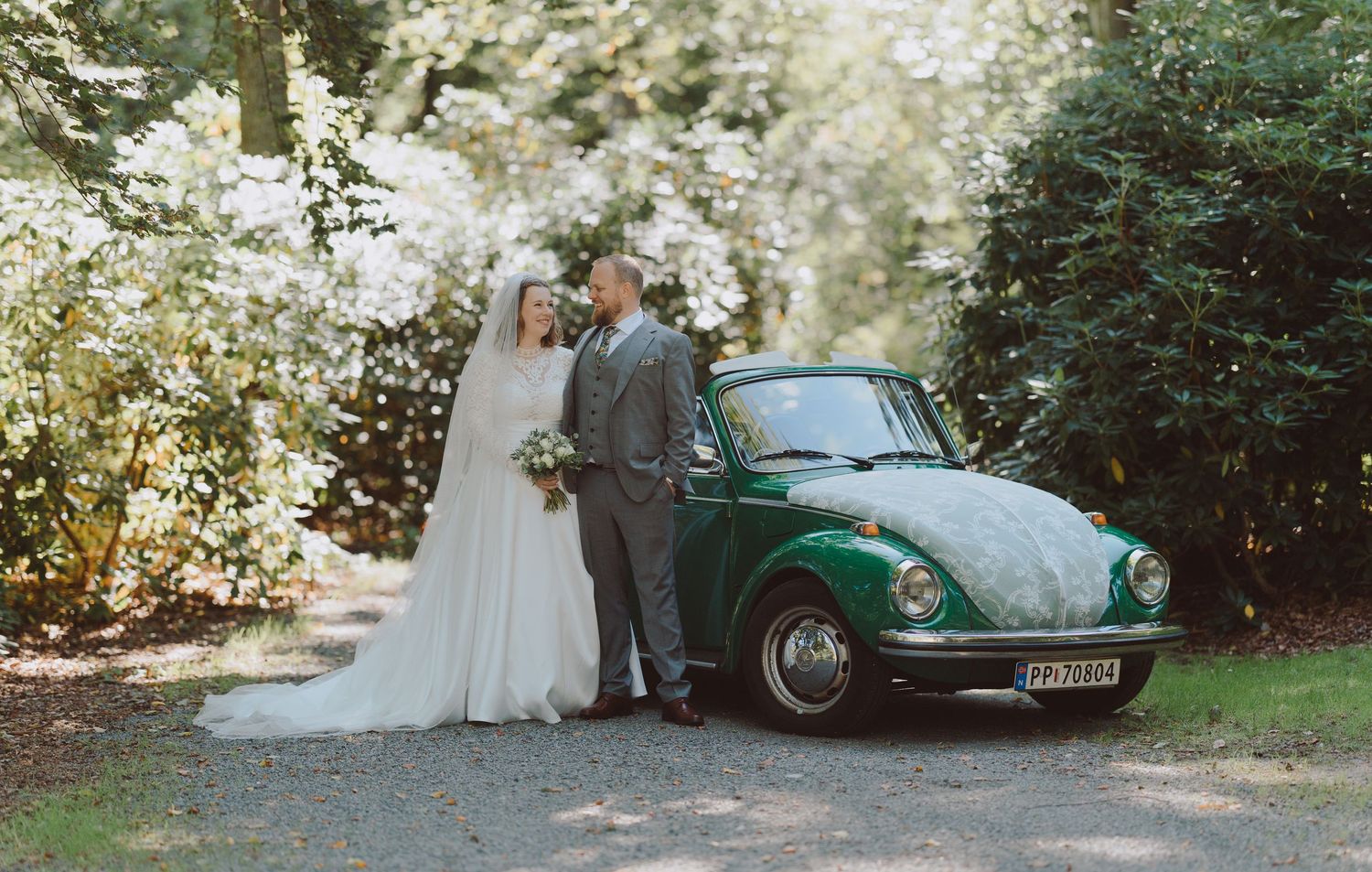 Newlyweds pose beside a vintage green Volkswagen Beetle on their wedding day.