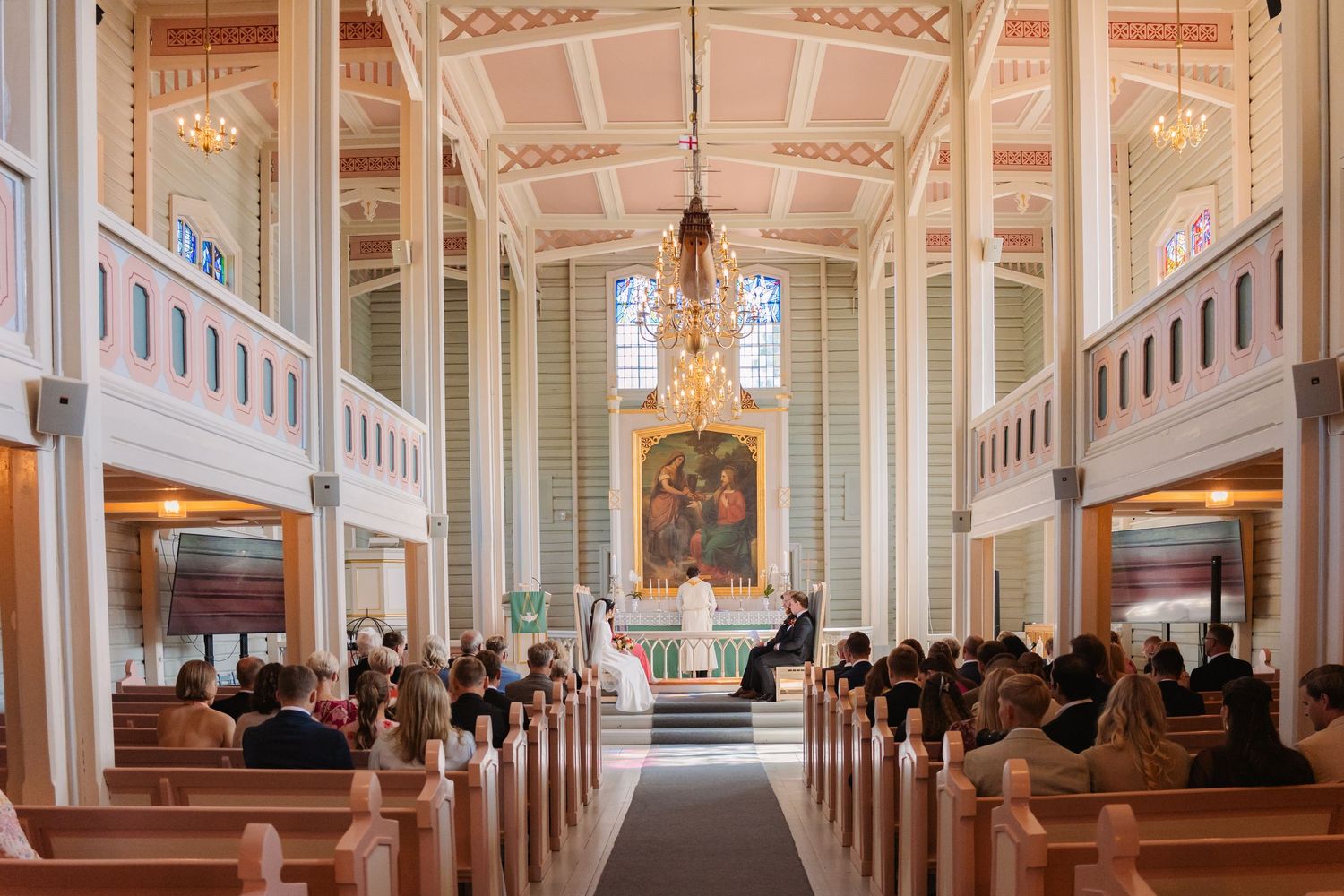 Interior view of a grand cathedral with ornate white columns, vaulted ceilings, and elegant chandeliers illuminating the space.