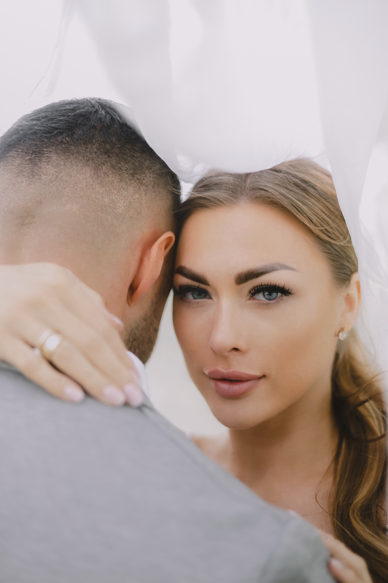 Romantic couple sharing intimate moment in soft lighting with elegant makeup and formal styling.