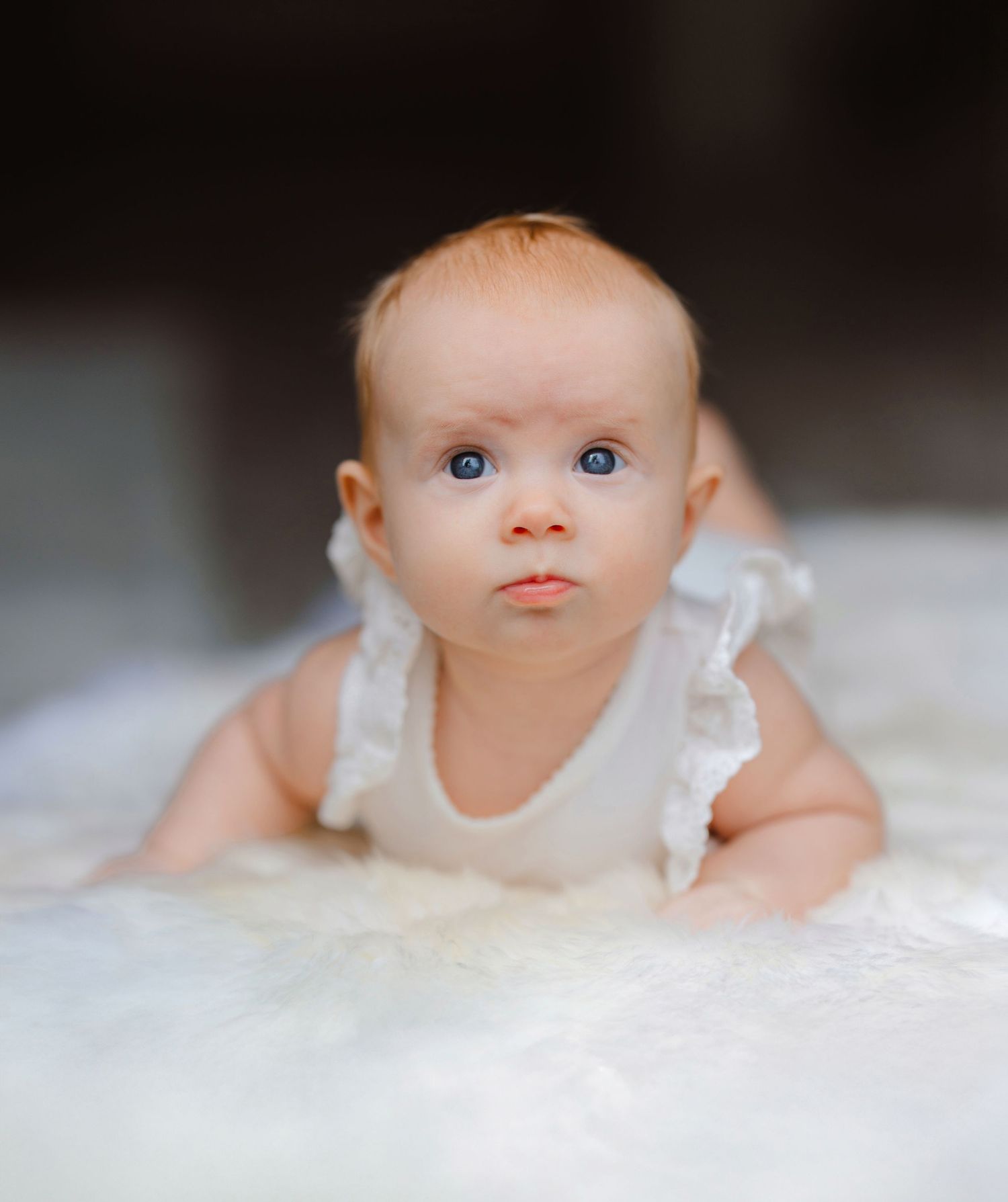 A baby wearing white lace clothing looks upward with soft focus creating a dreamy portrait series.