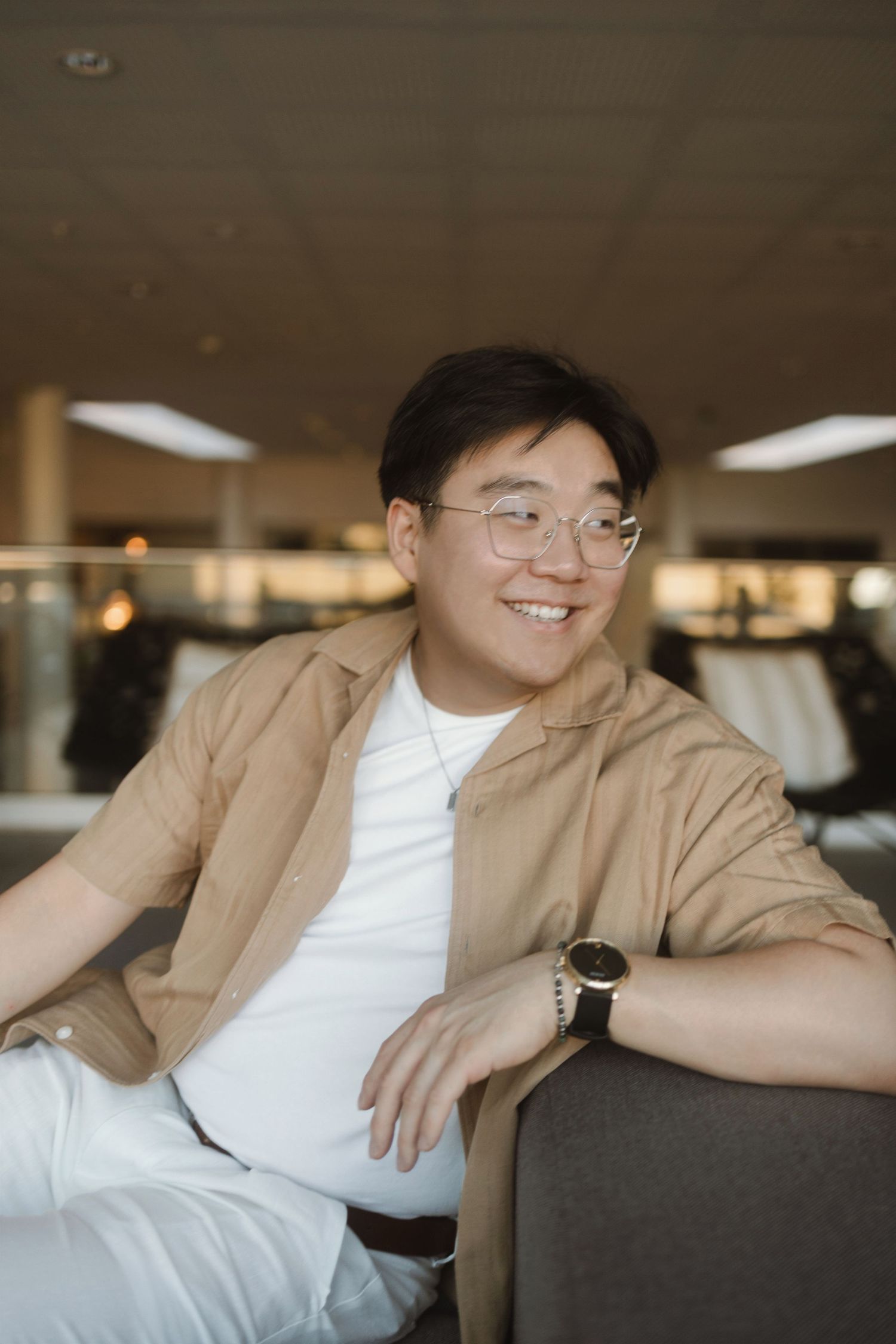 A person in a tan blazer and white shirt relaxes on a couch with a casual, laid-back pose.