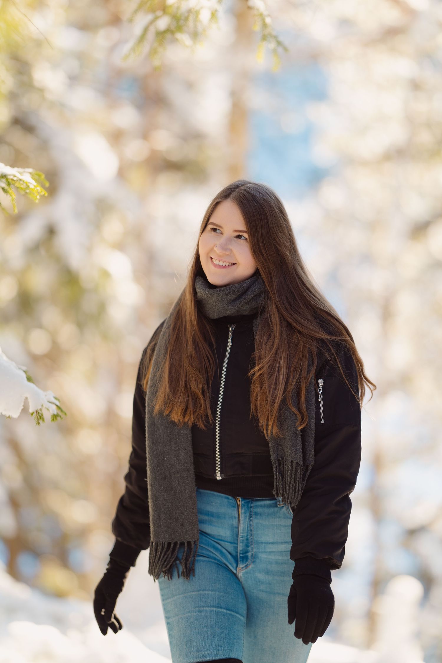 A person in a black jacket and denim poses playfully against a snowy winter backdrop.