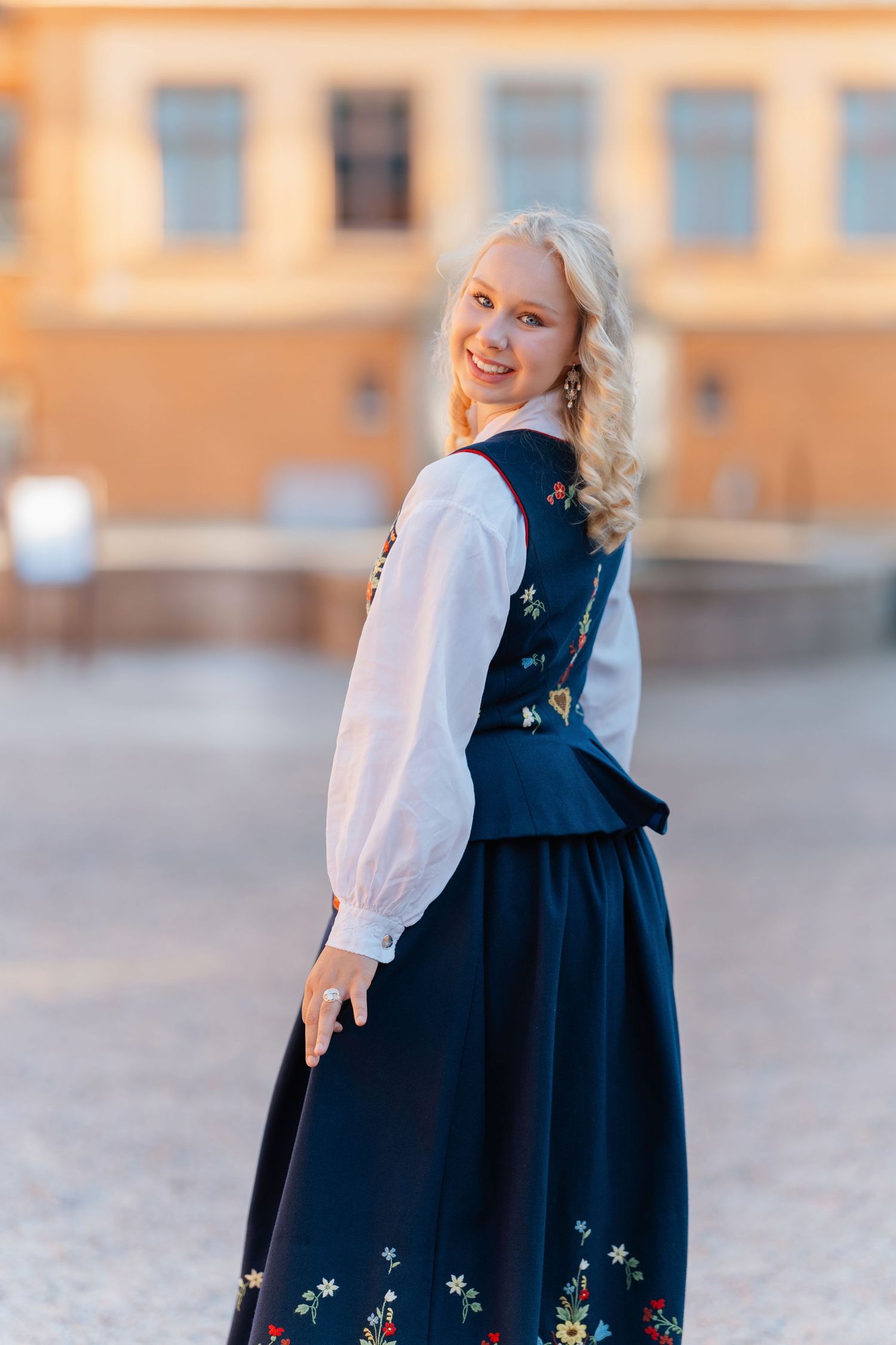 Young blonde woman smiling in traditional Nordic embroidered navy dress and white blouse outdoors.