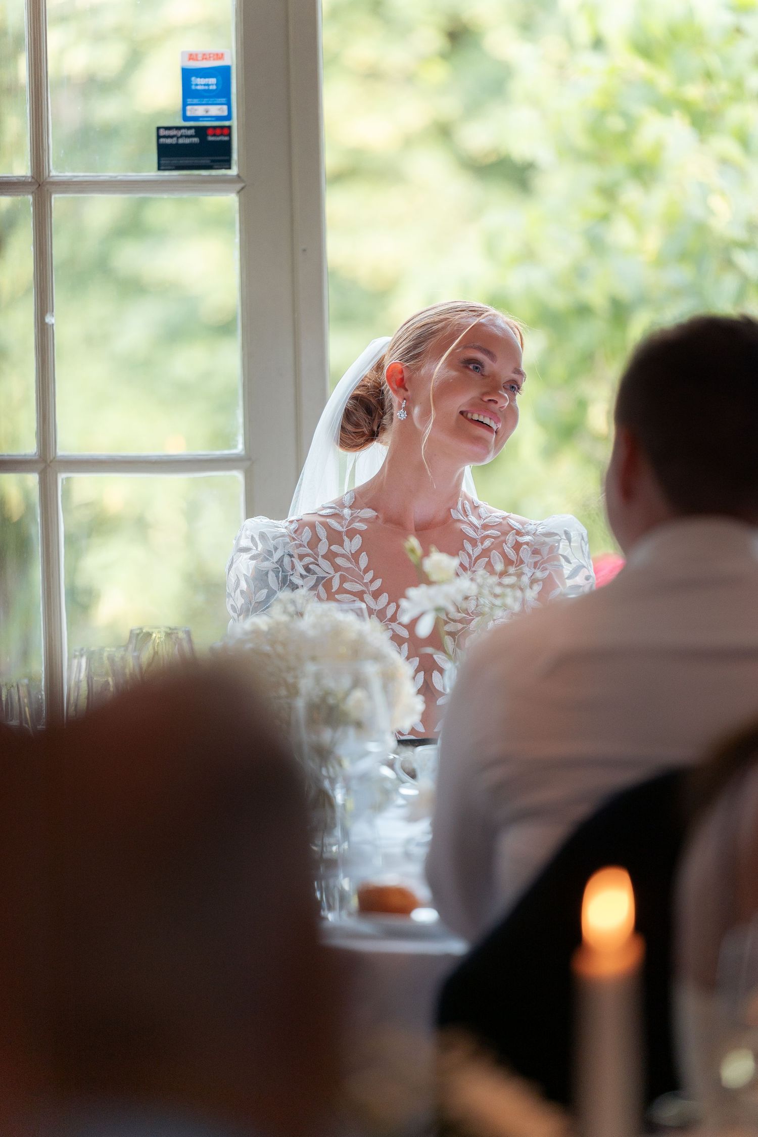 A bride in a white lace dress laughs joyfully during a wedding reception indoors.