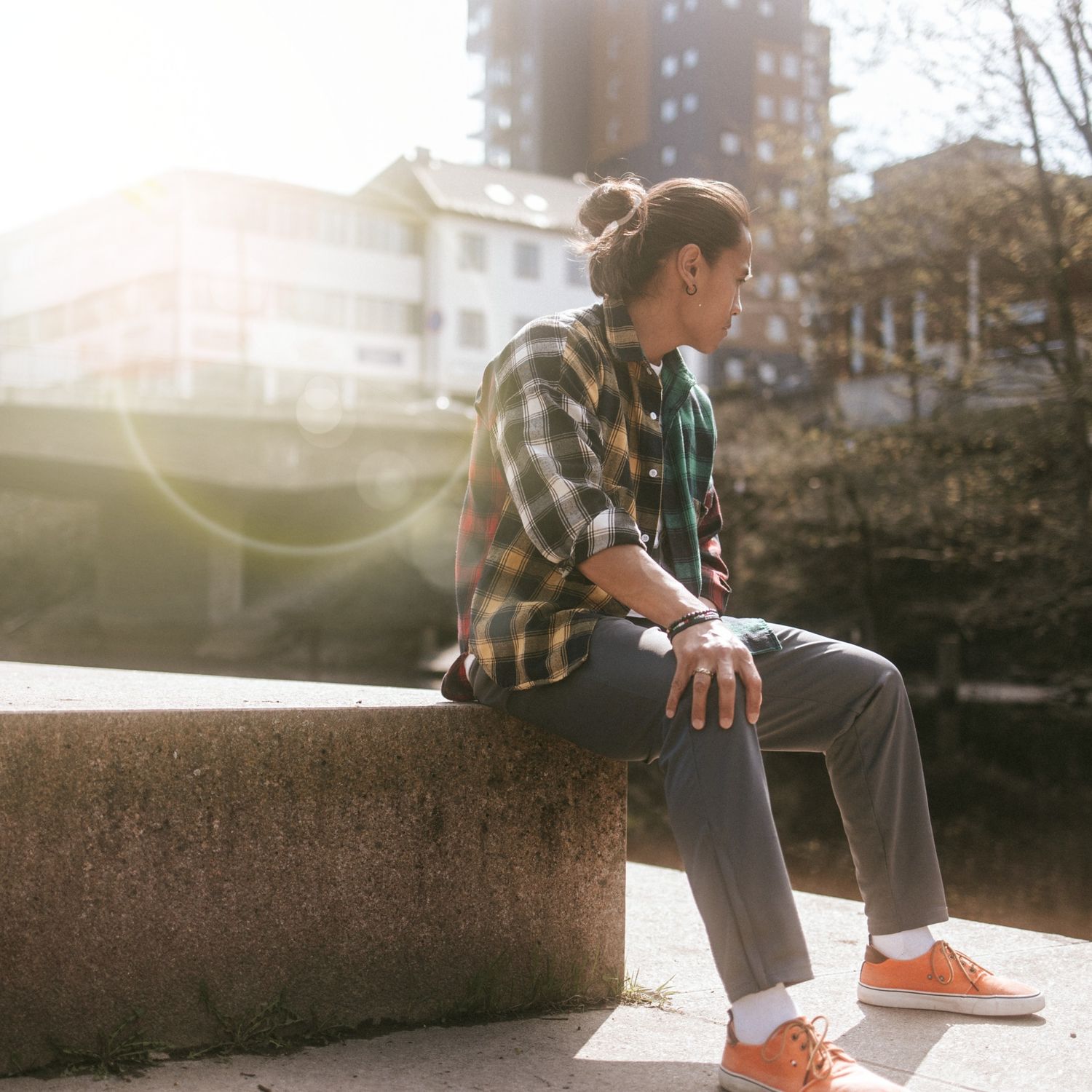 Person in plaid shirt sitting on concrete ledge with orange sneakers in warm sunlight during golden hour.