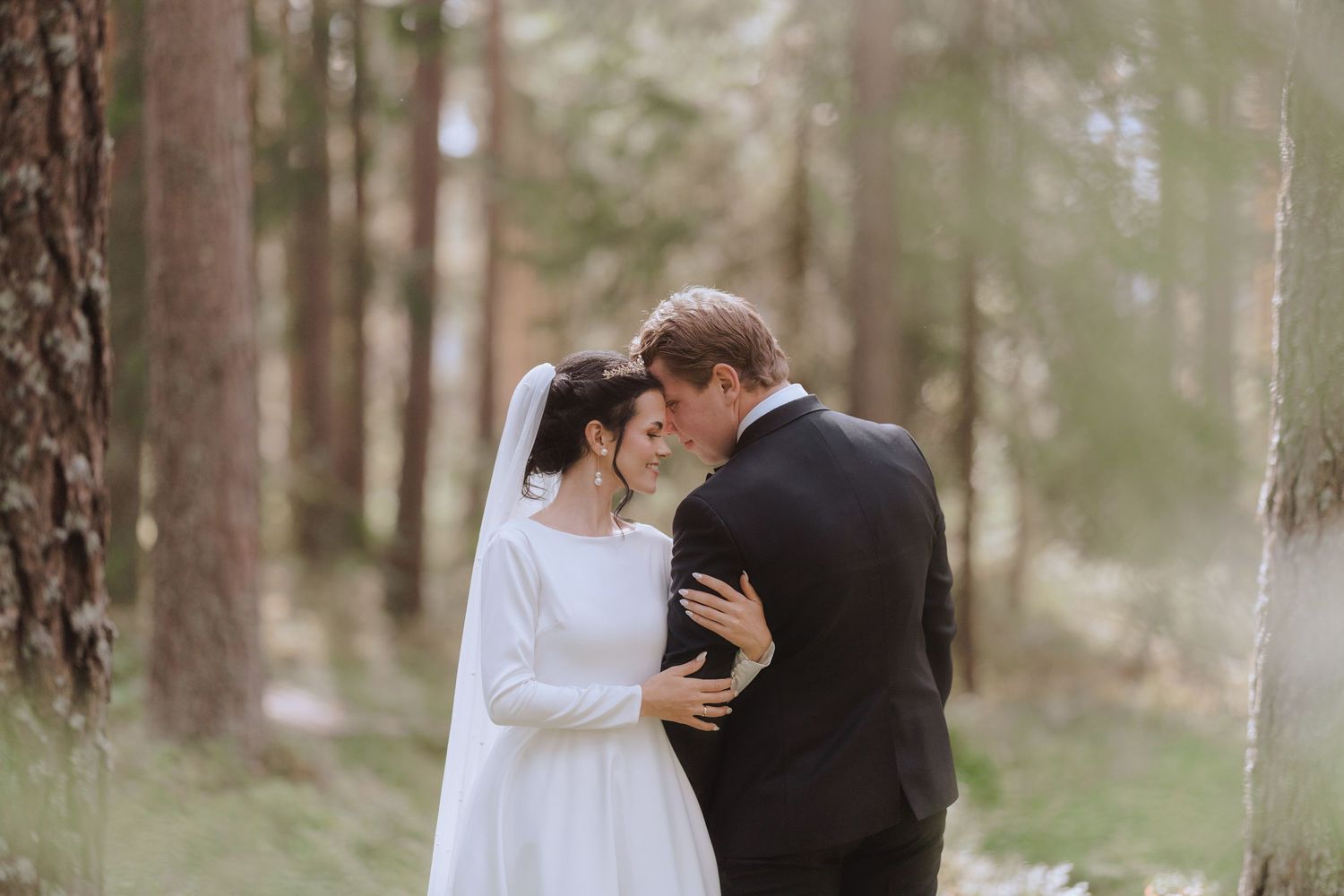 A couple in wedding attire shares an intimate moment together in a misty forest setting.