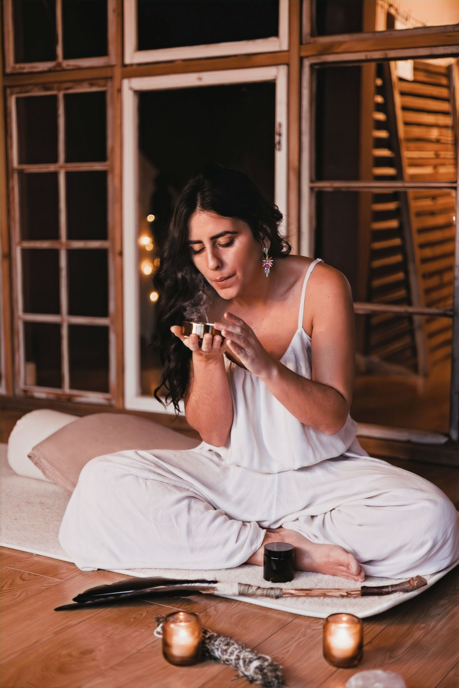 Person in white pajamas sitting with candles and reading in evening setting.