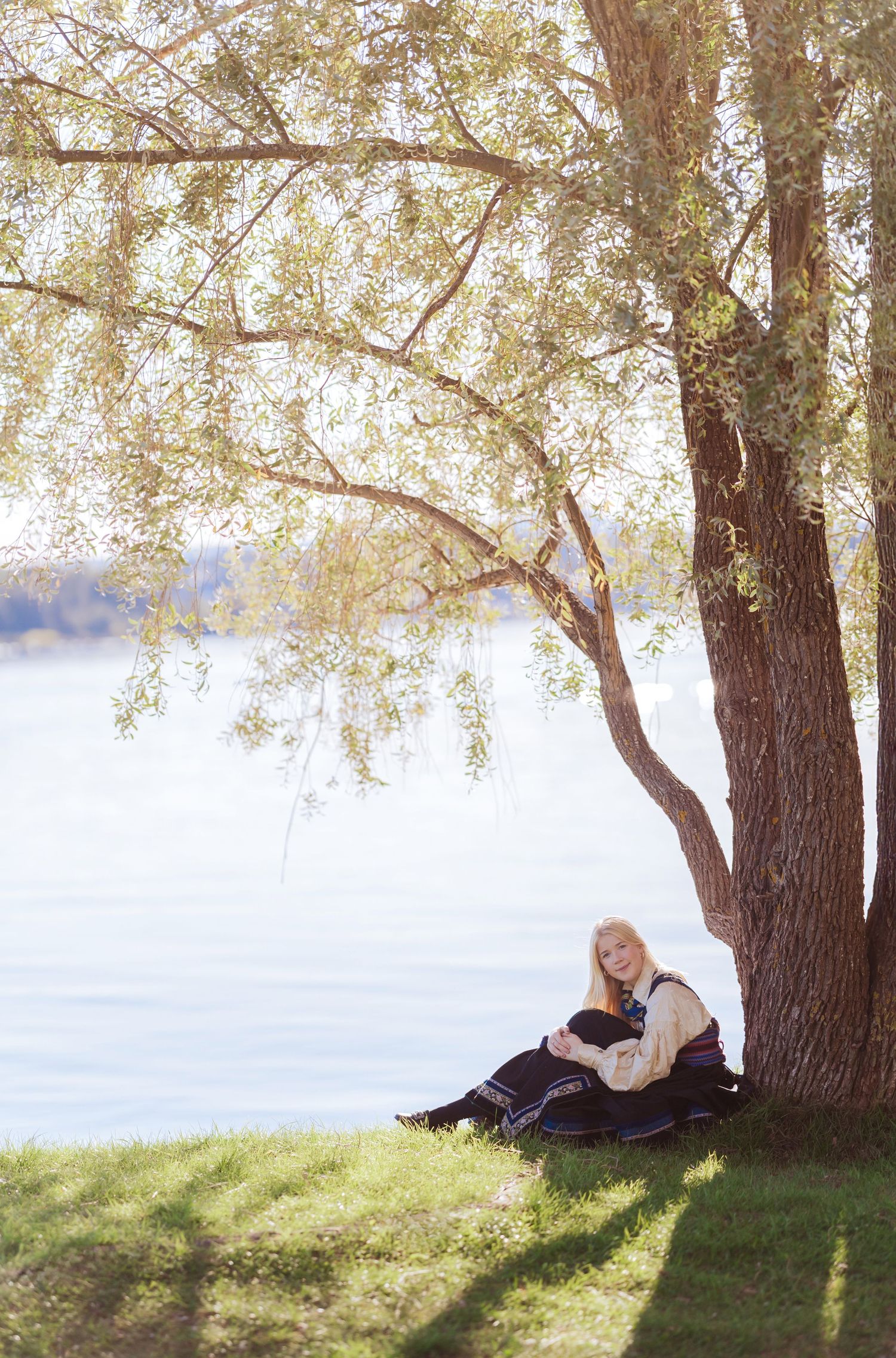 Four sequential photos show someone relaxing under a tree on a sunny day by a lake, creating a peaceful nature scene.