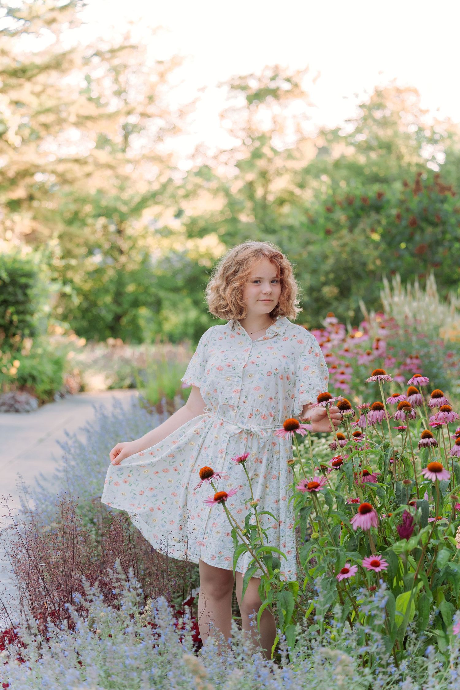 A floral dress twirls among pink and red wildflowers in a dreamy garden setting at sunset.