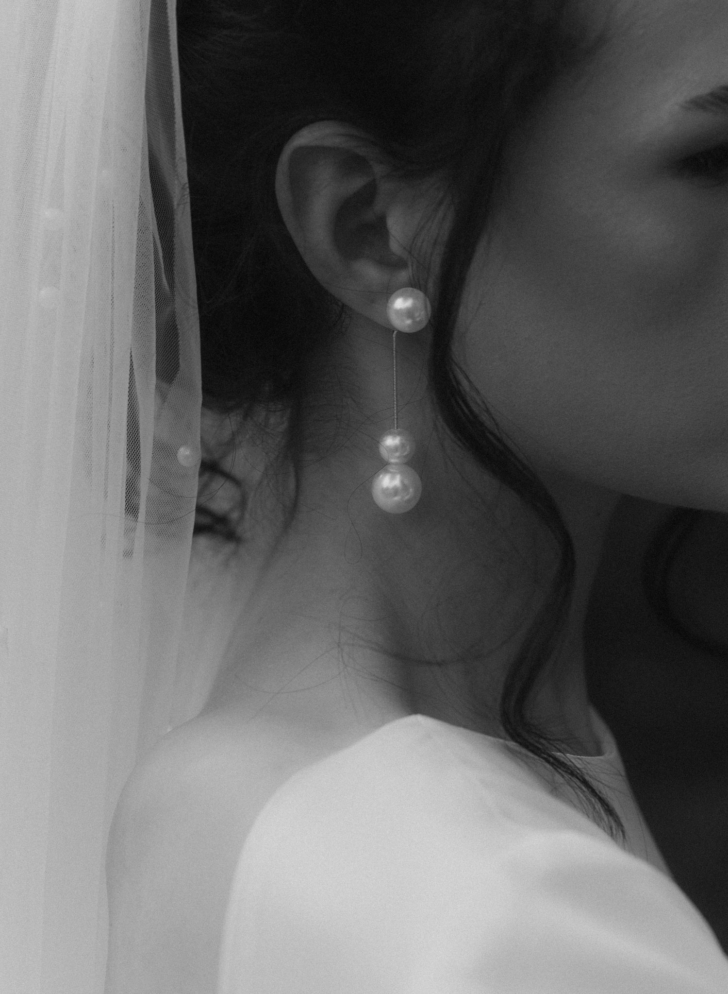Black and white portrait photograph of a bride wearing a veil and pearl earrings in an elegant pose.