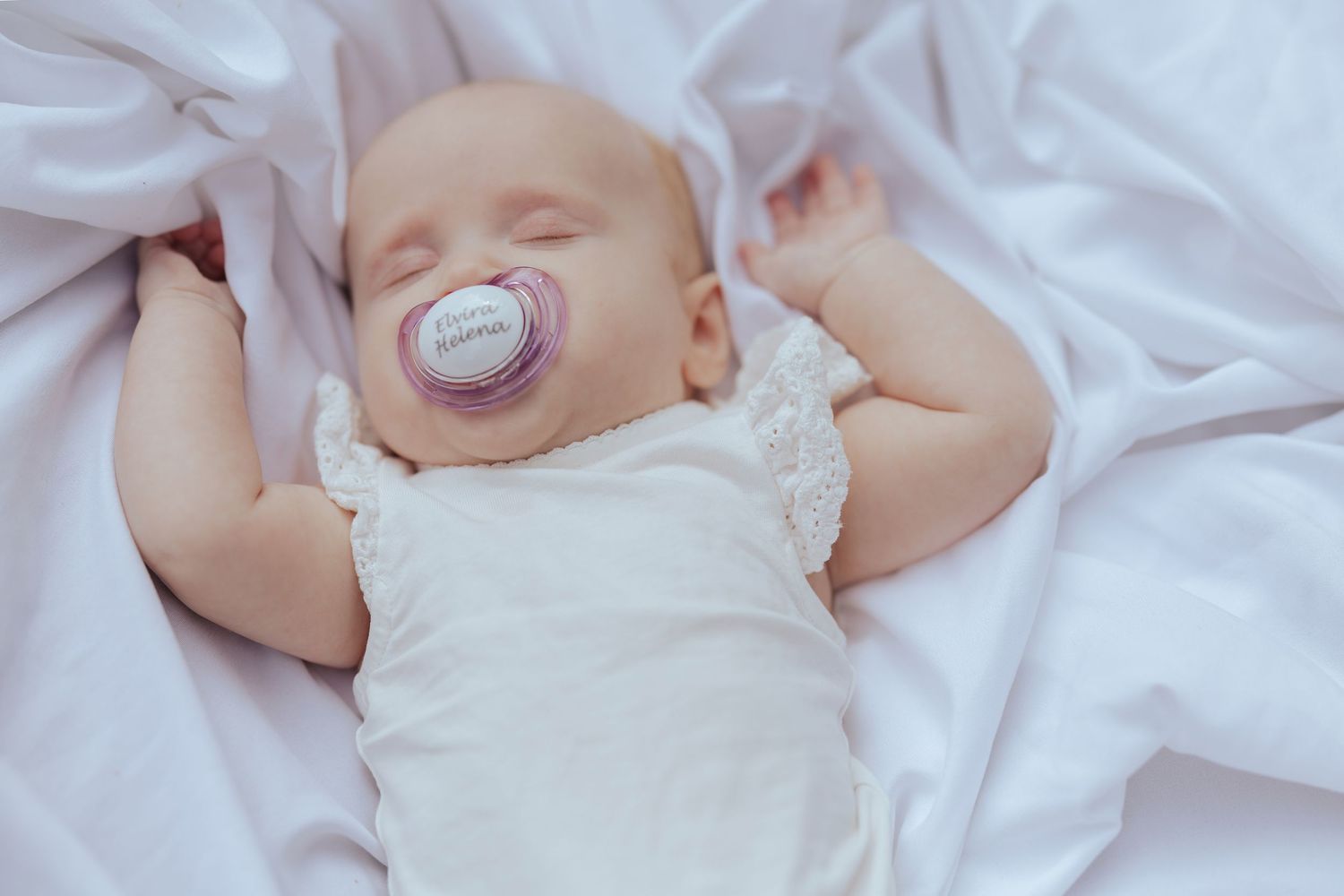 Adorable newborn baby wrapped in white blankets smiling while sleeping peacefully on soft bedding.