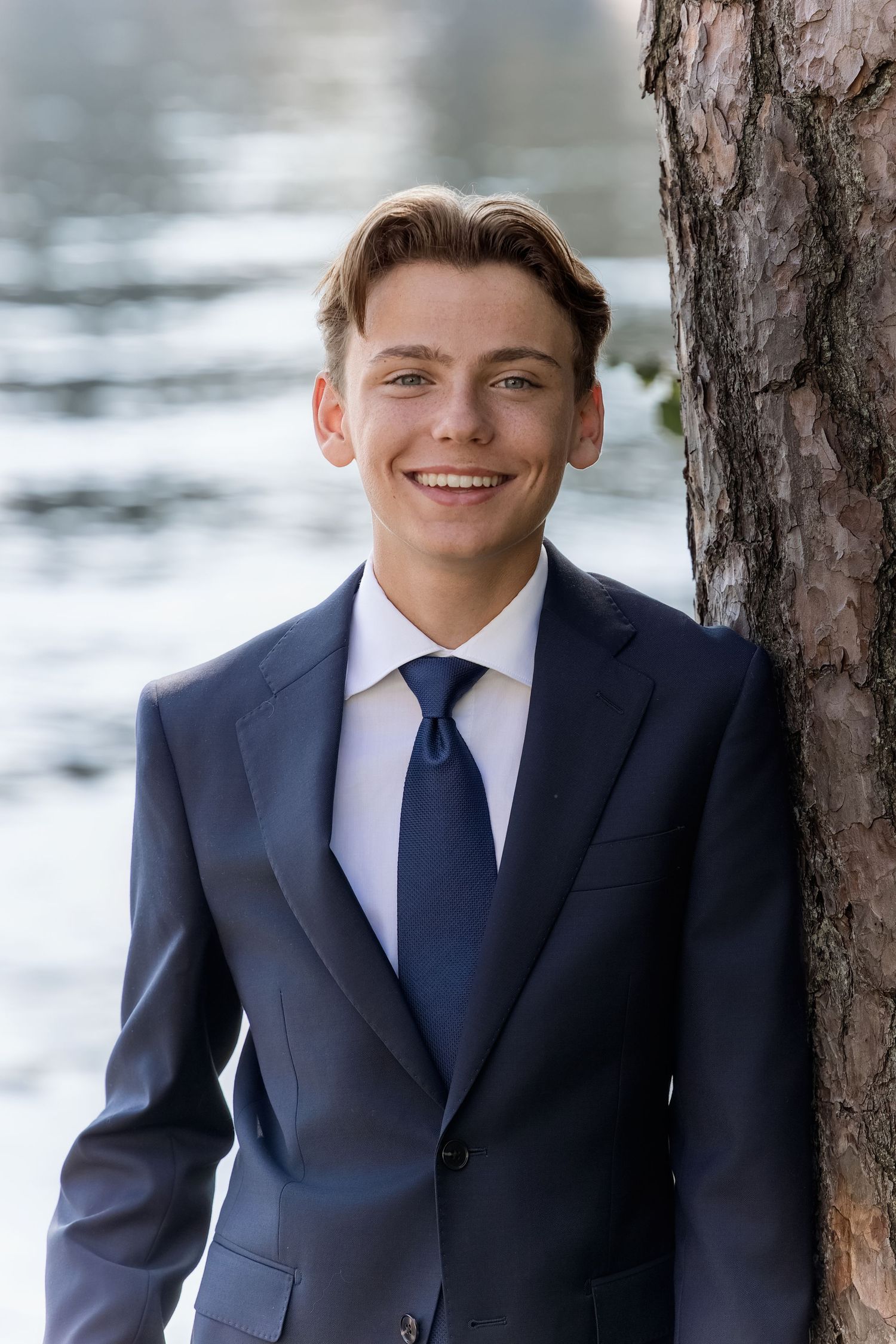 A sequence of four professional headshots showing someone in a navy suit and tie against a blurred outdoor background.