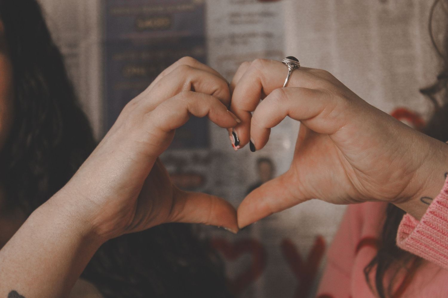 Two people forming a heart shape with their hands, one wearing a diamond engagement ring.