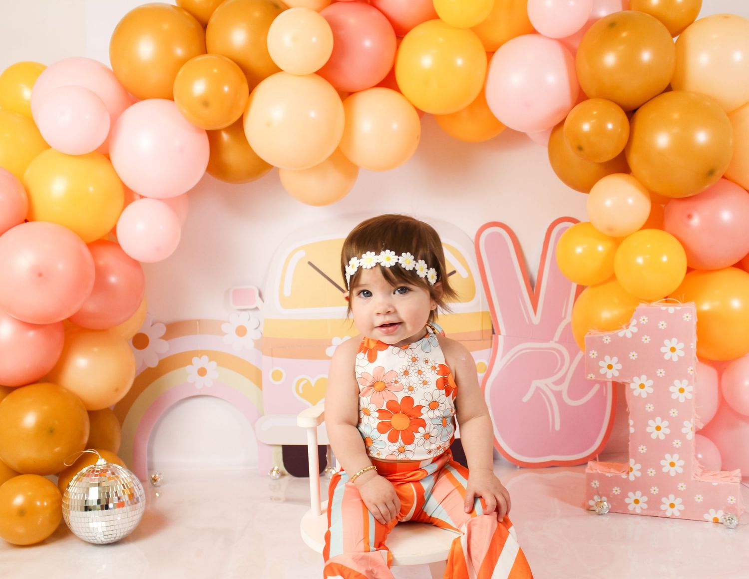 Baby girl in floral outfit at groovy retro peace sign first birthday cake smash session.