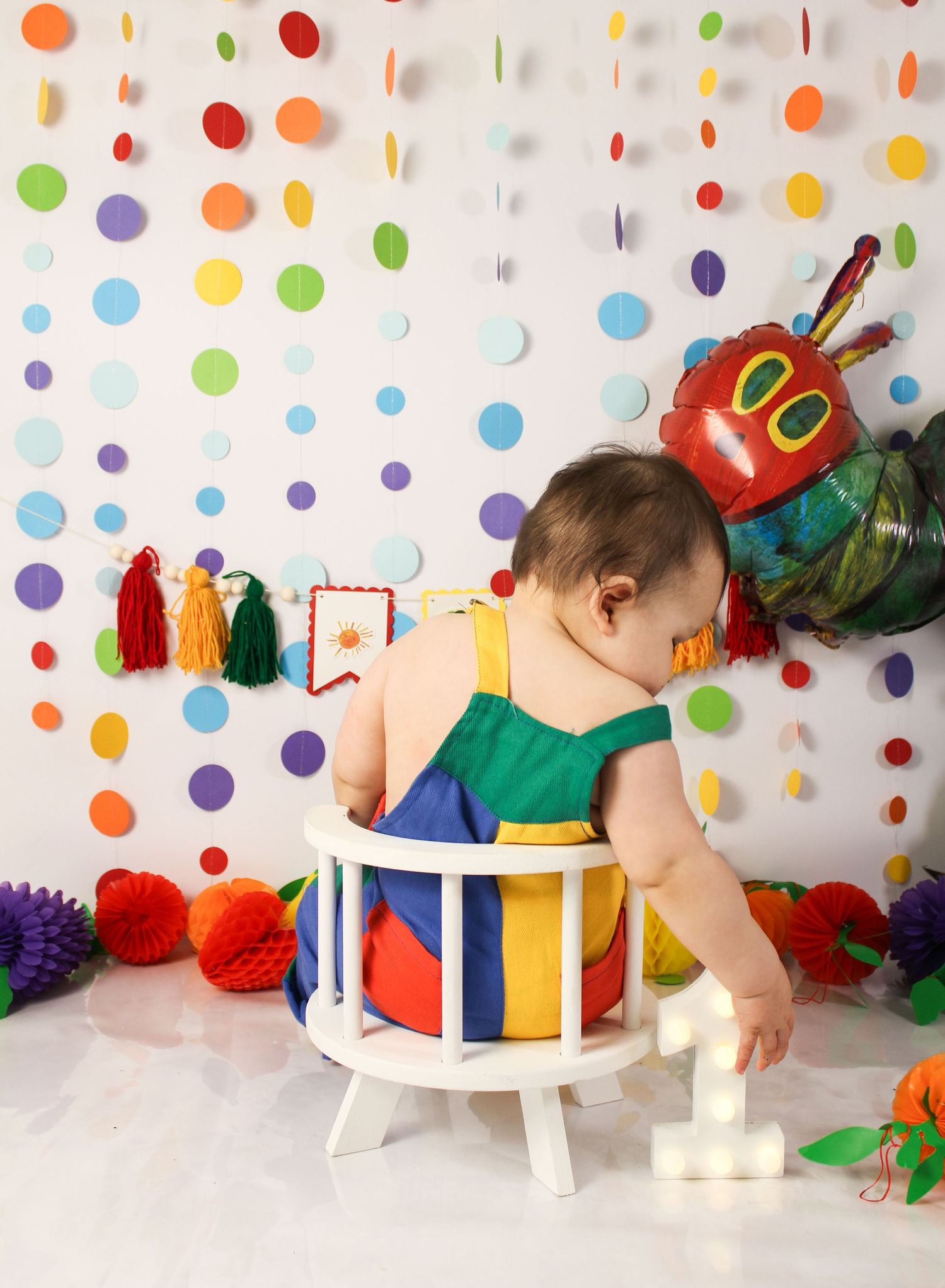 Baby in colorful outfit at Very Hungry Caterpillar themed first birthday cake smash session.