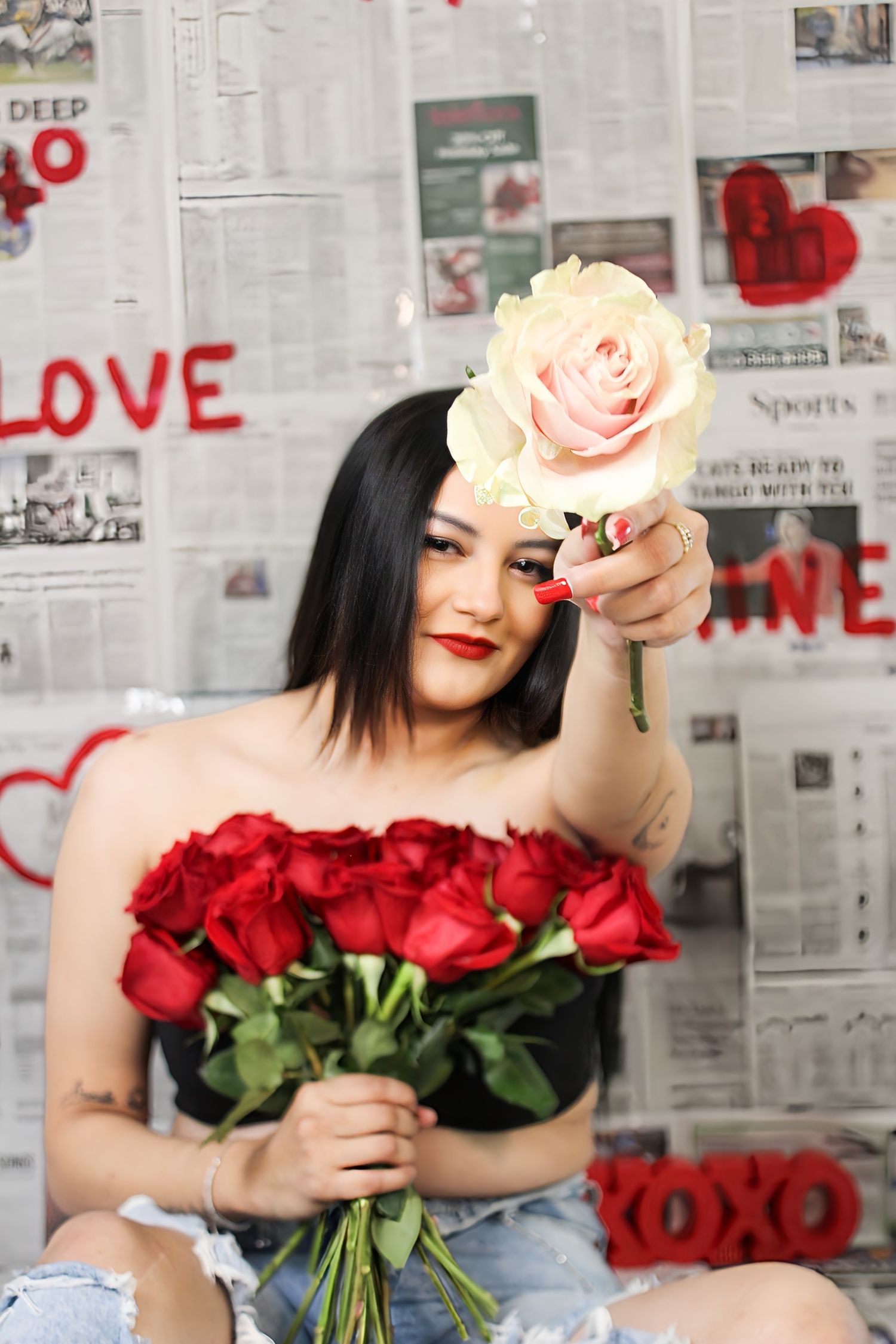 A woman with red lips holds red roses and extends a white rose toward the camera on a Valentine's Day backdrop.