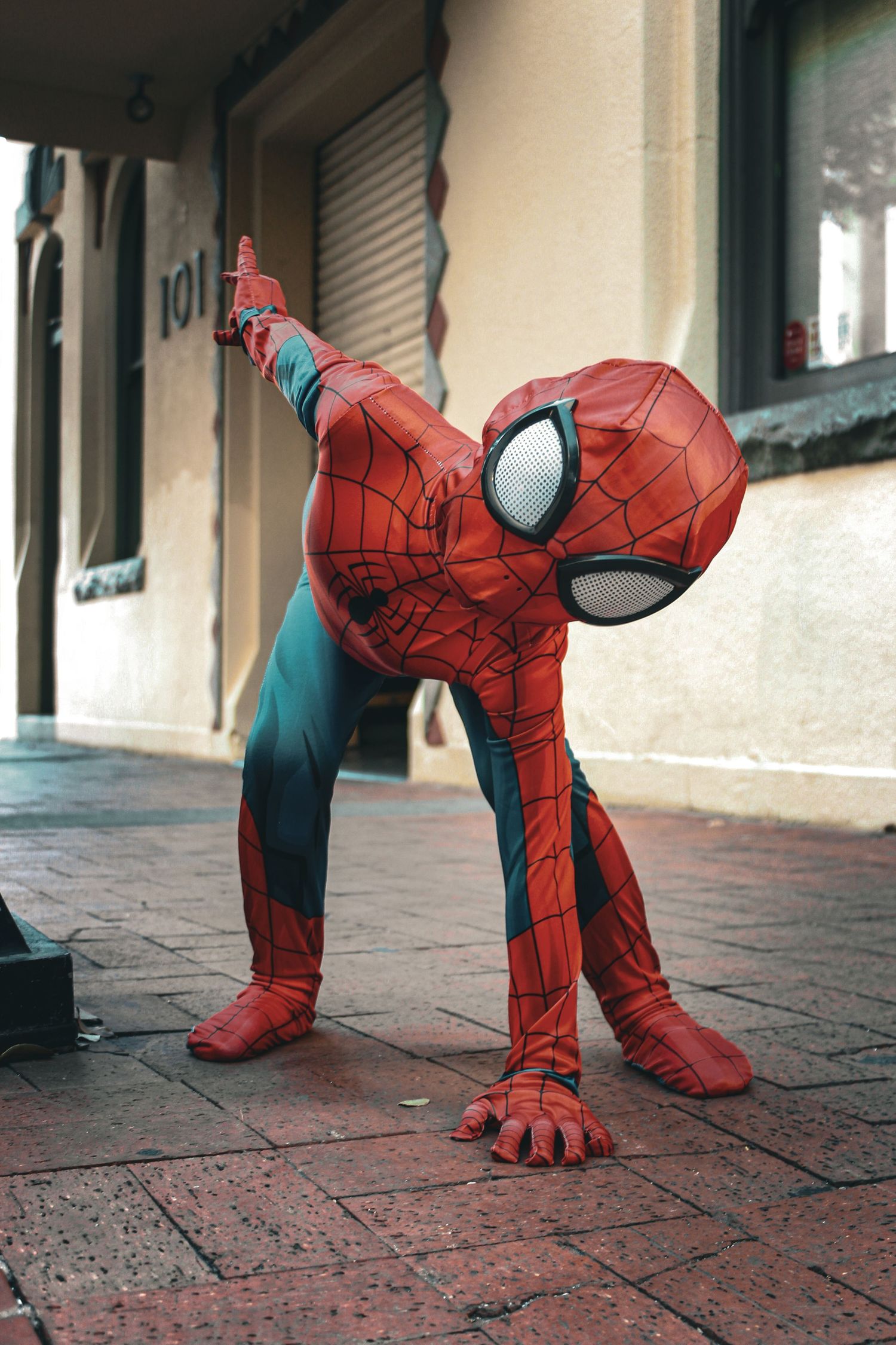 Child in Spider-Man costume doing a dramatic pose on a brick sidewalk.