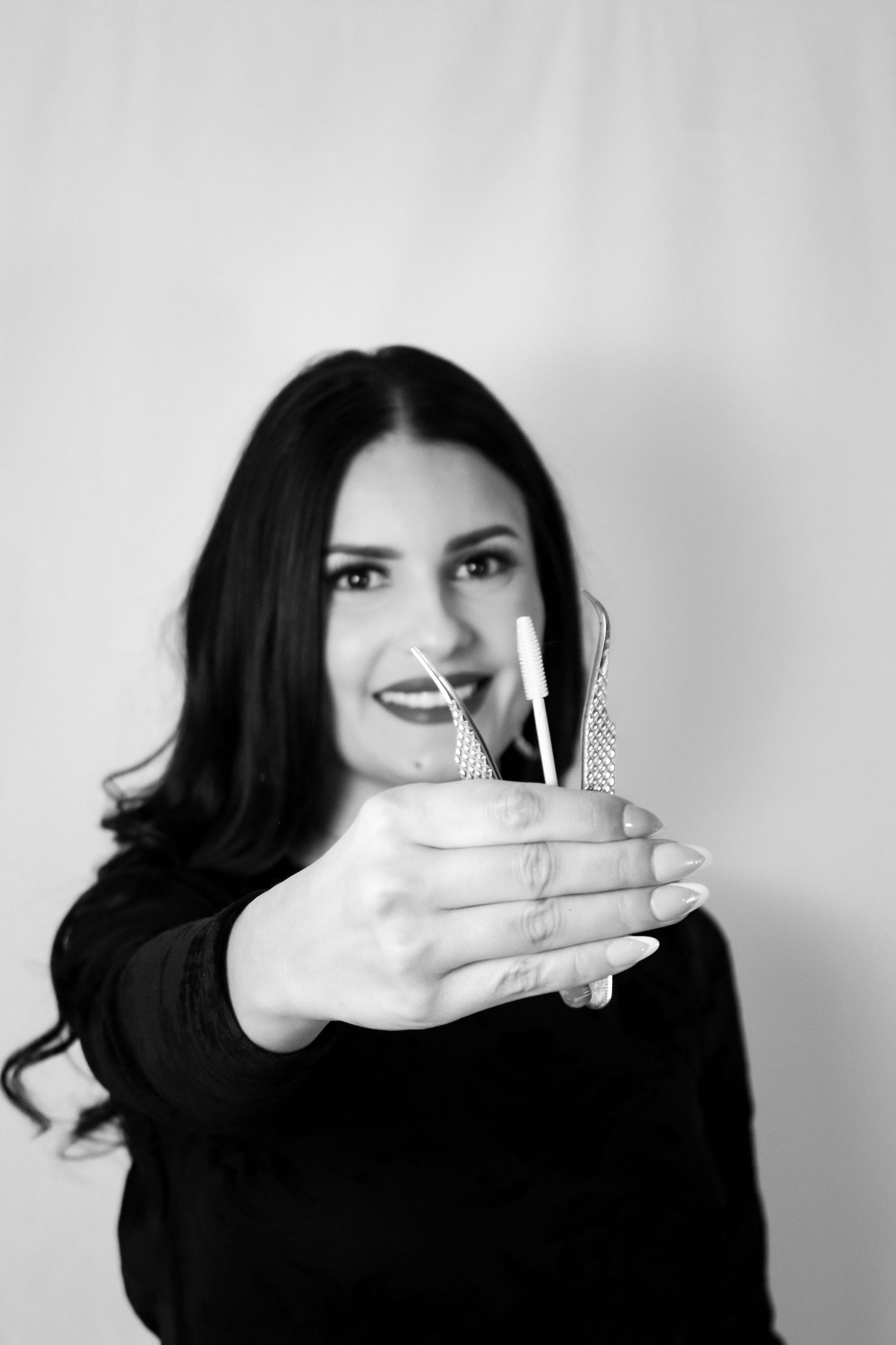 Black and white close-up of a smiling dark-haired woman extending dental instruments toward the camera.