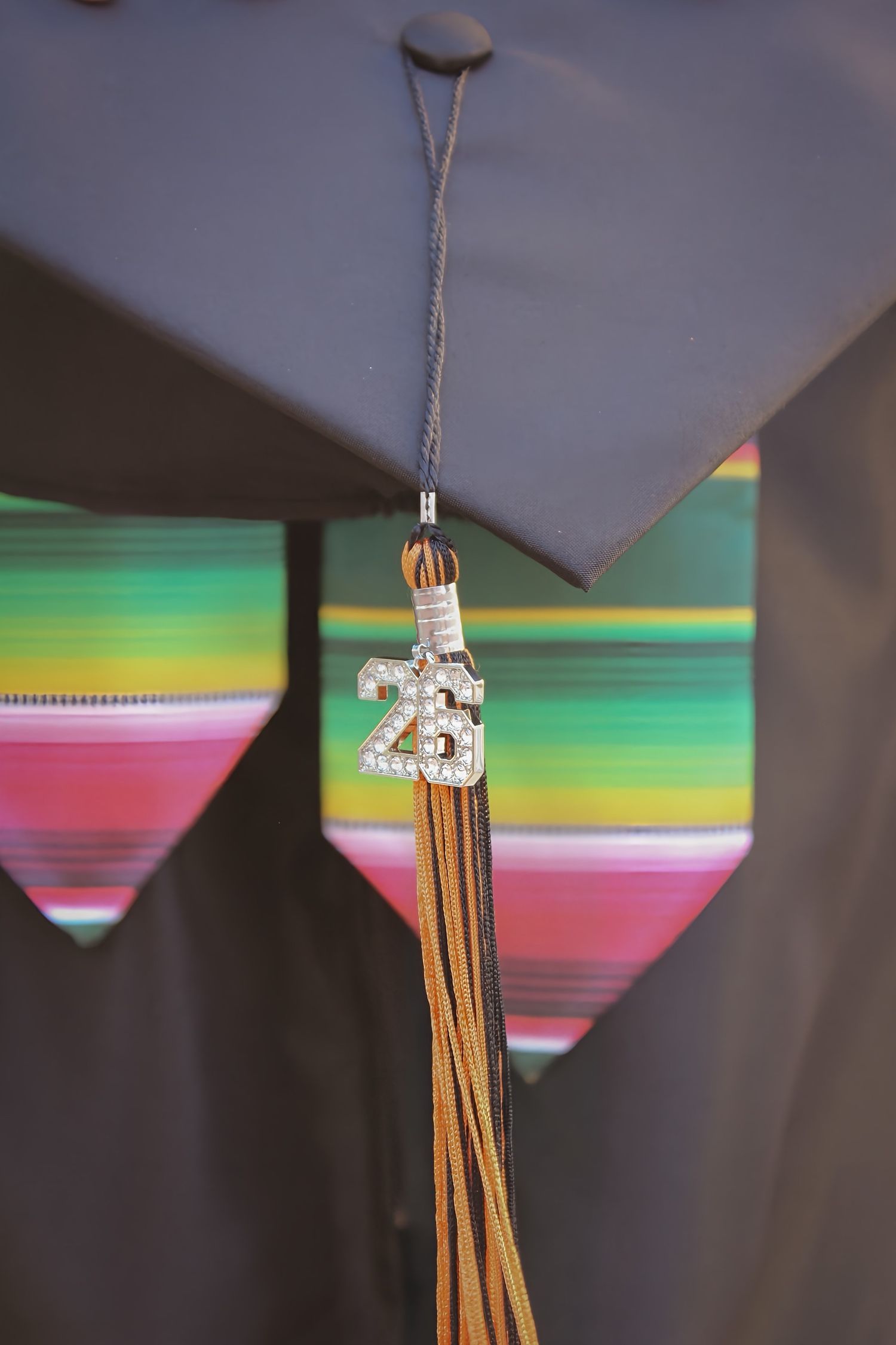 Close-up of a graduation cap tassel with a rhinestone '25' charm against a colorful serape background.