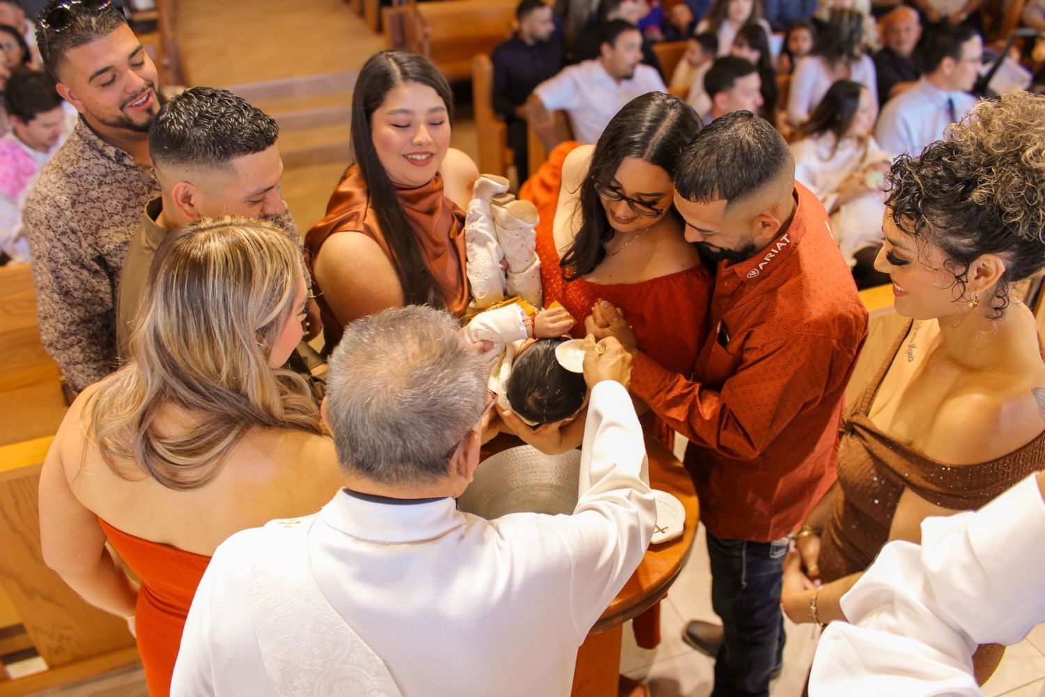 Family and friends gathered around baby during baptism ceremony inside a church.