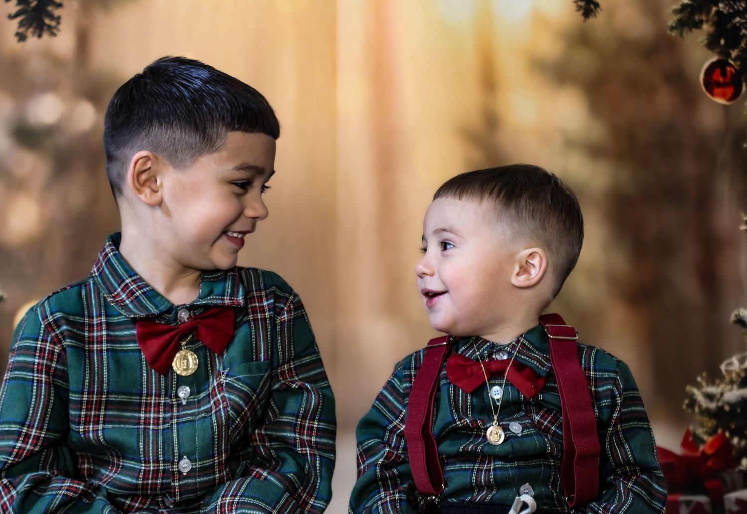 Two young boys in matching green plaid Christmas outfits smile at each other in a holiday portrait.