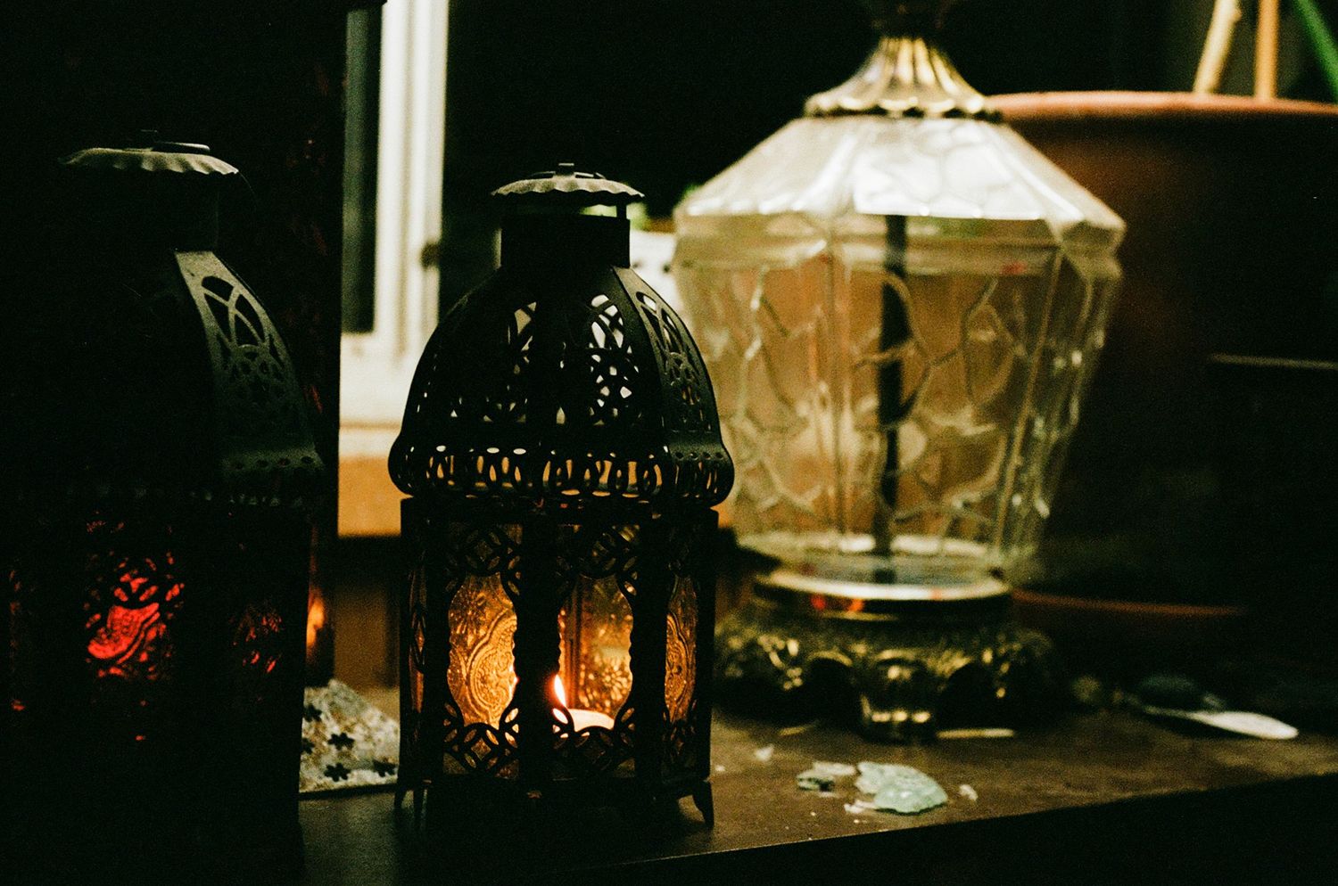 Two ornate candle lanterns flicker softly next to a beautiful glass vase in a windowsill, a calming still life snapshot.