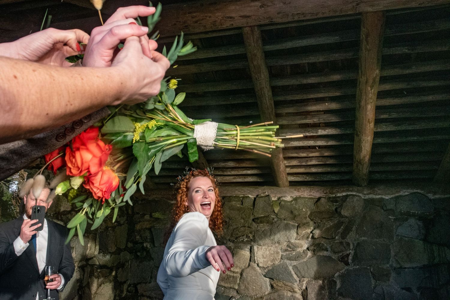 A newlywed bride beaming with joy looks back to see the hands of her best friends' clasped in midair around the bouquet she has just thrown