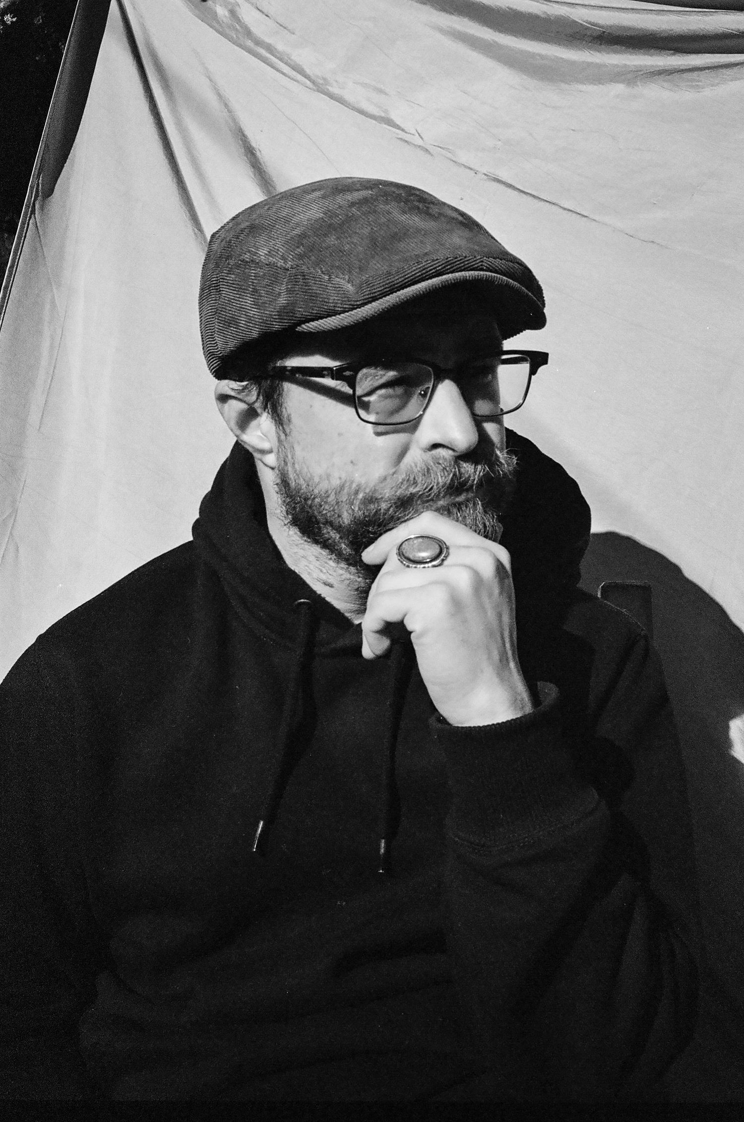 The artist himself poses pensively in this monochromatic frame, wearing a ring and newsboy cap.